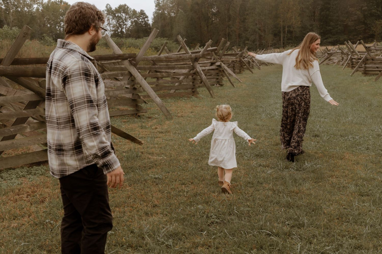 Candid family interaction in rustic outdoor setting with wooden fencing.