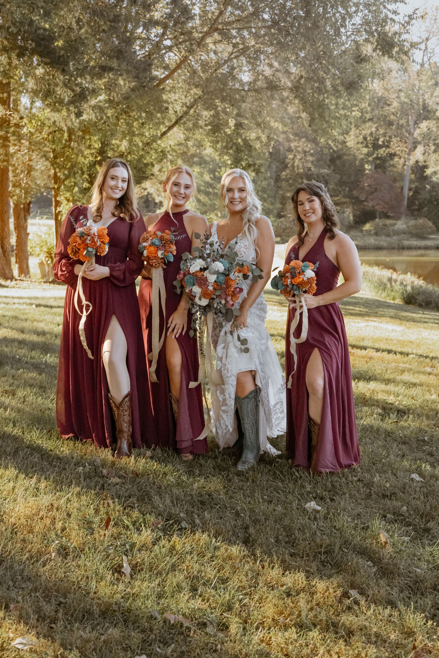 Bridesmaids in burgundy dresses pose together on grassy hill during fall wedding.