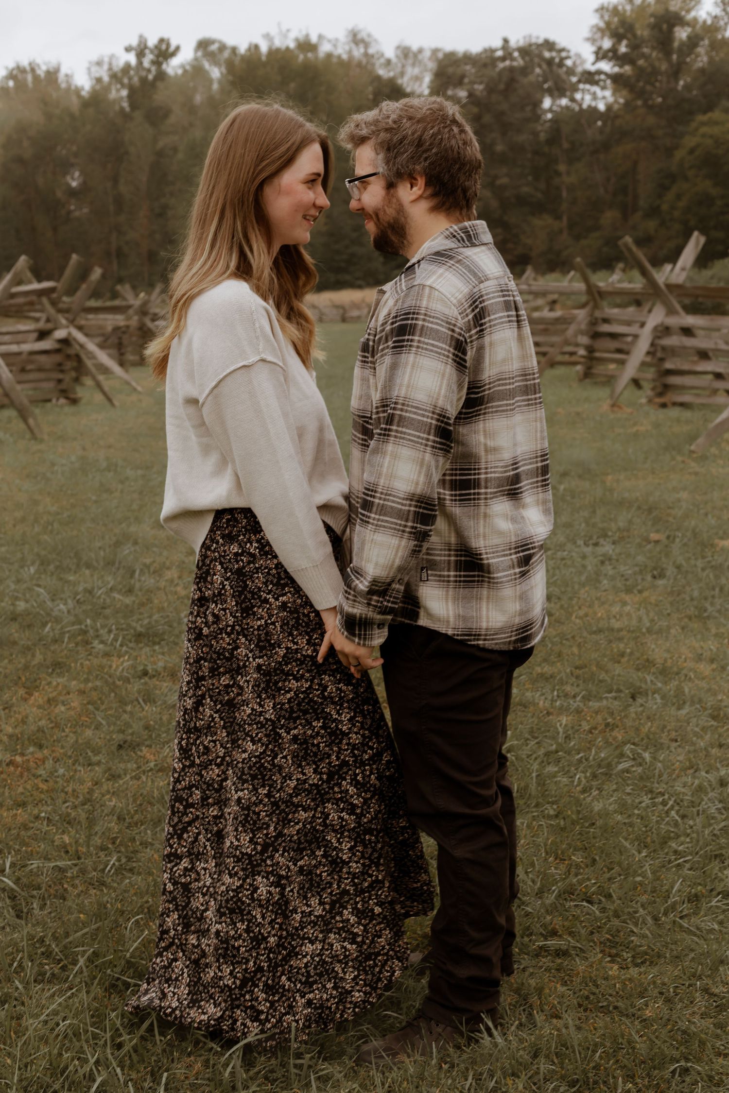 Family members stand together in a grassy field near rustic wooden fencing.