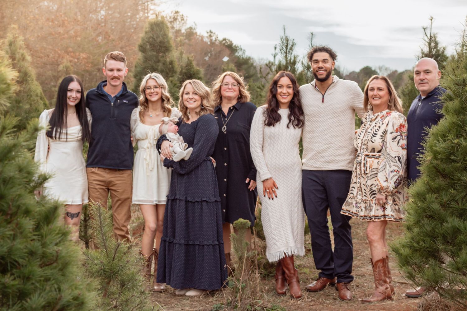Extended family gathering for a group photo among pine trees in coordinated outfits.