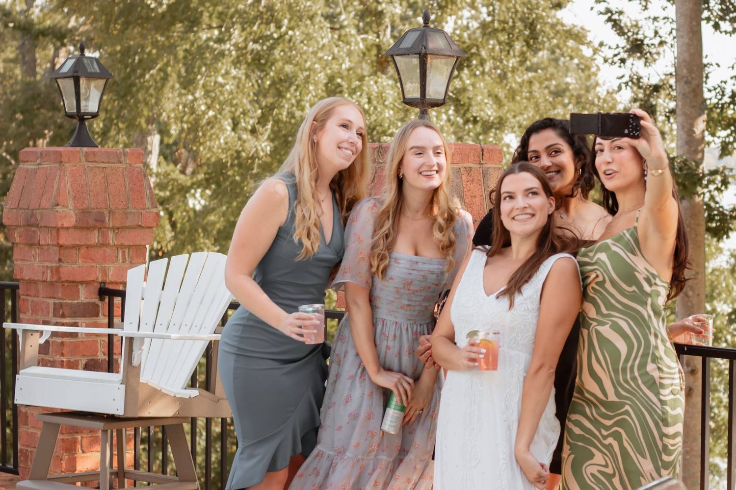 Bridesmaids in mixed gray and sage dresses socialize during outdoor reception.