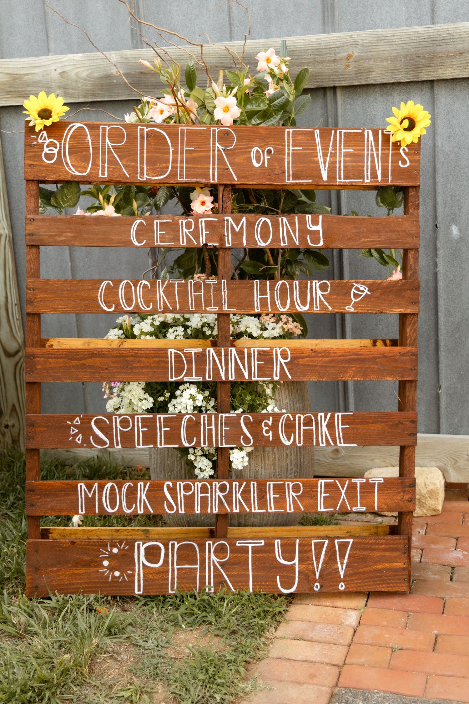 Rustic wooden pallet wedding sign displaying order of events including ceremony, cocktail hour, dinner, speeches, cake, and party.