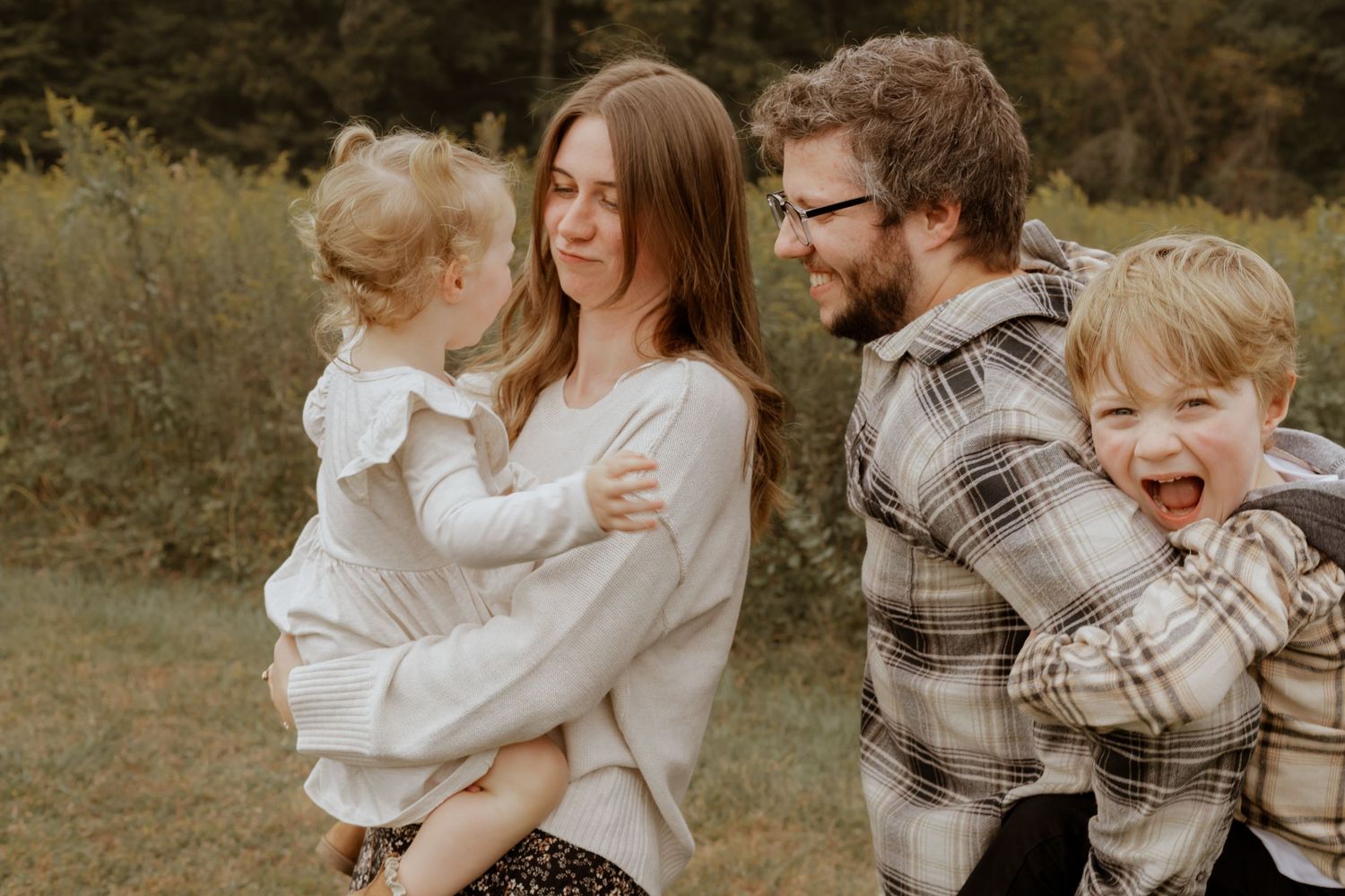 A family enjoys a candid outdoor photo session in coordinated neutral outfits on a fall day.