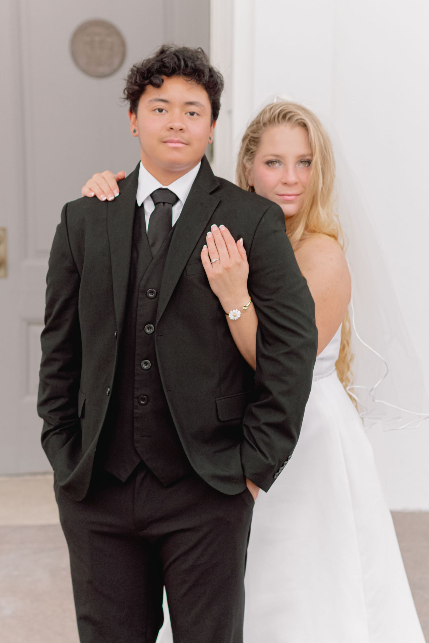 Elegant wedding couple poses formally against white pillars and classic architecture.