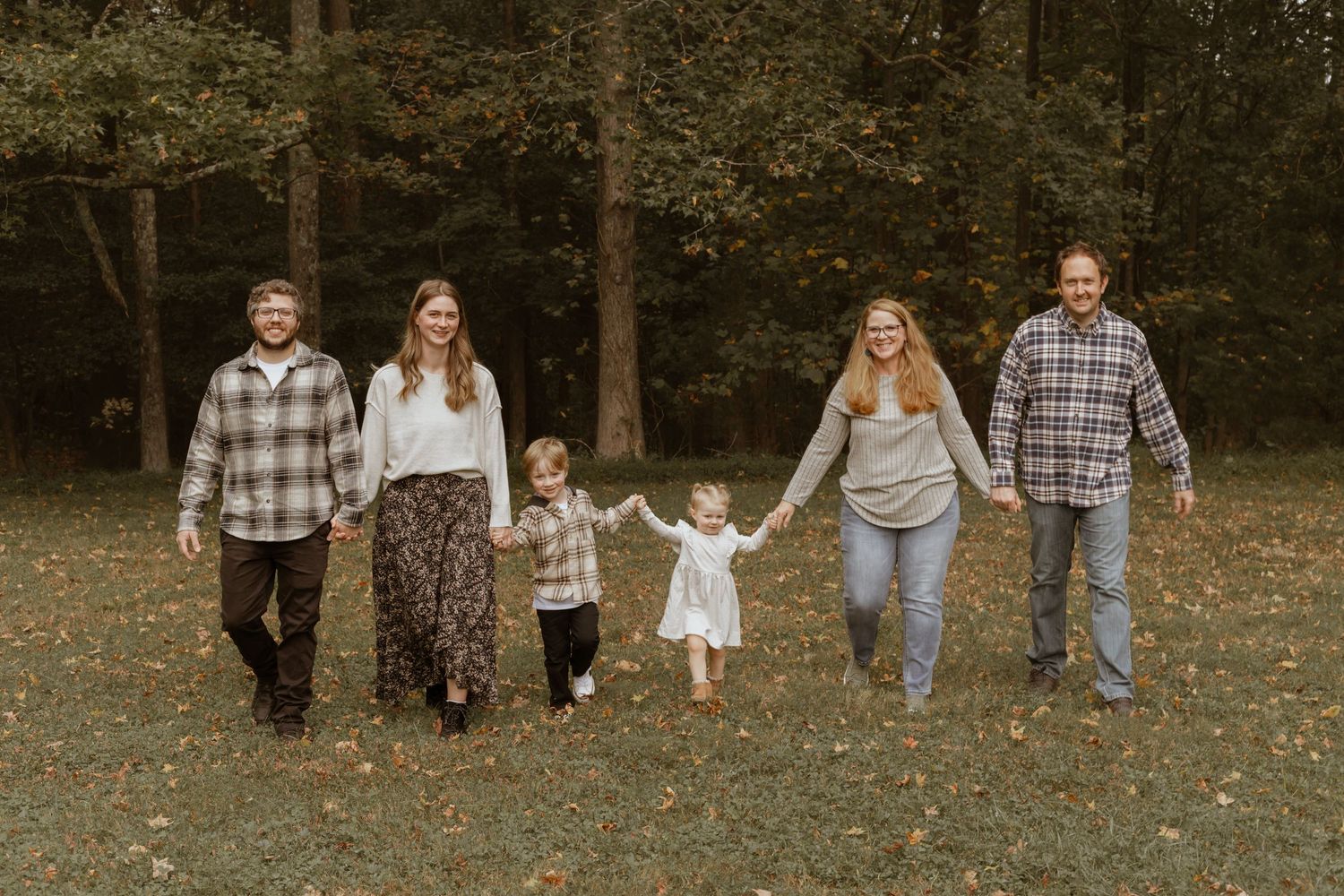 Family walking together hand in hand through a wooded area with fallen leaves.