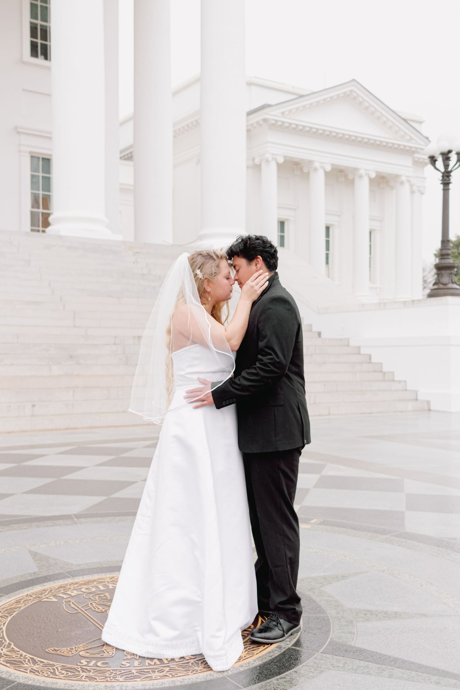 Newlyweds embrace in an intimate moment against a backdrop of classic white architecture.