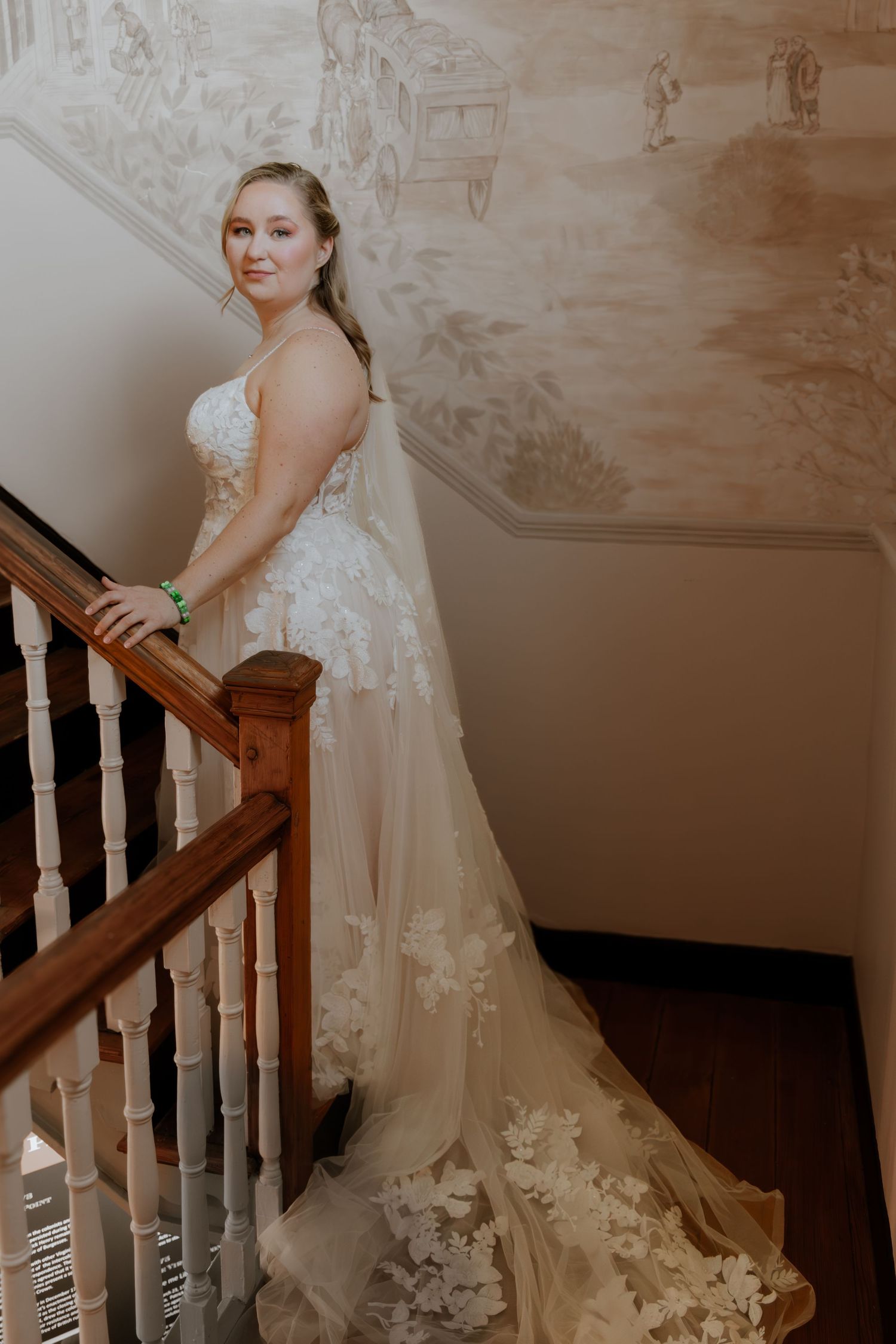 Bride in elegant lace wedding gown poses on vintage staircase.