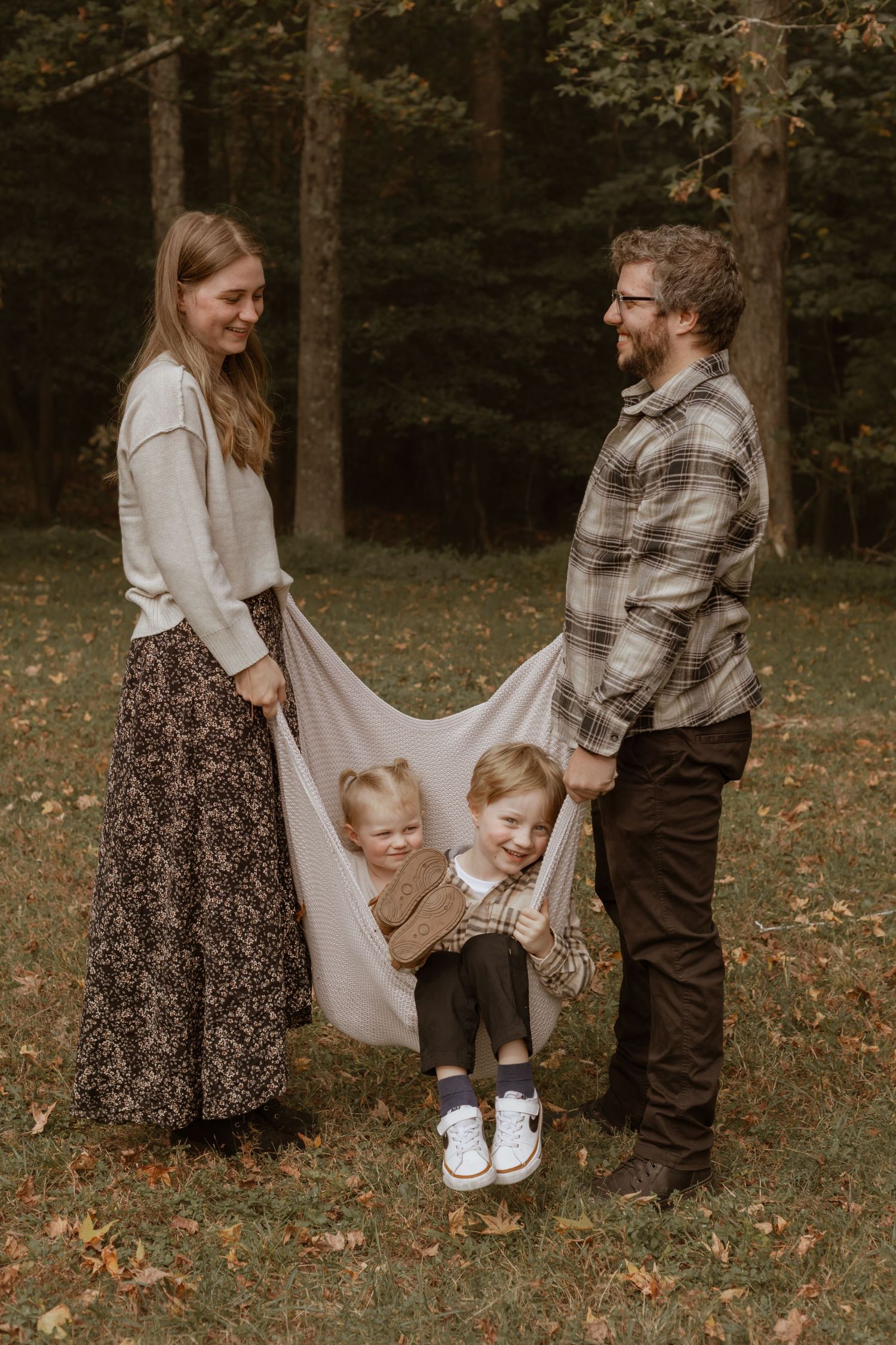 Family playing together with a white blanket in a fall forest setting.