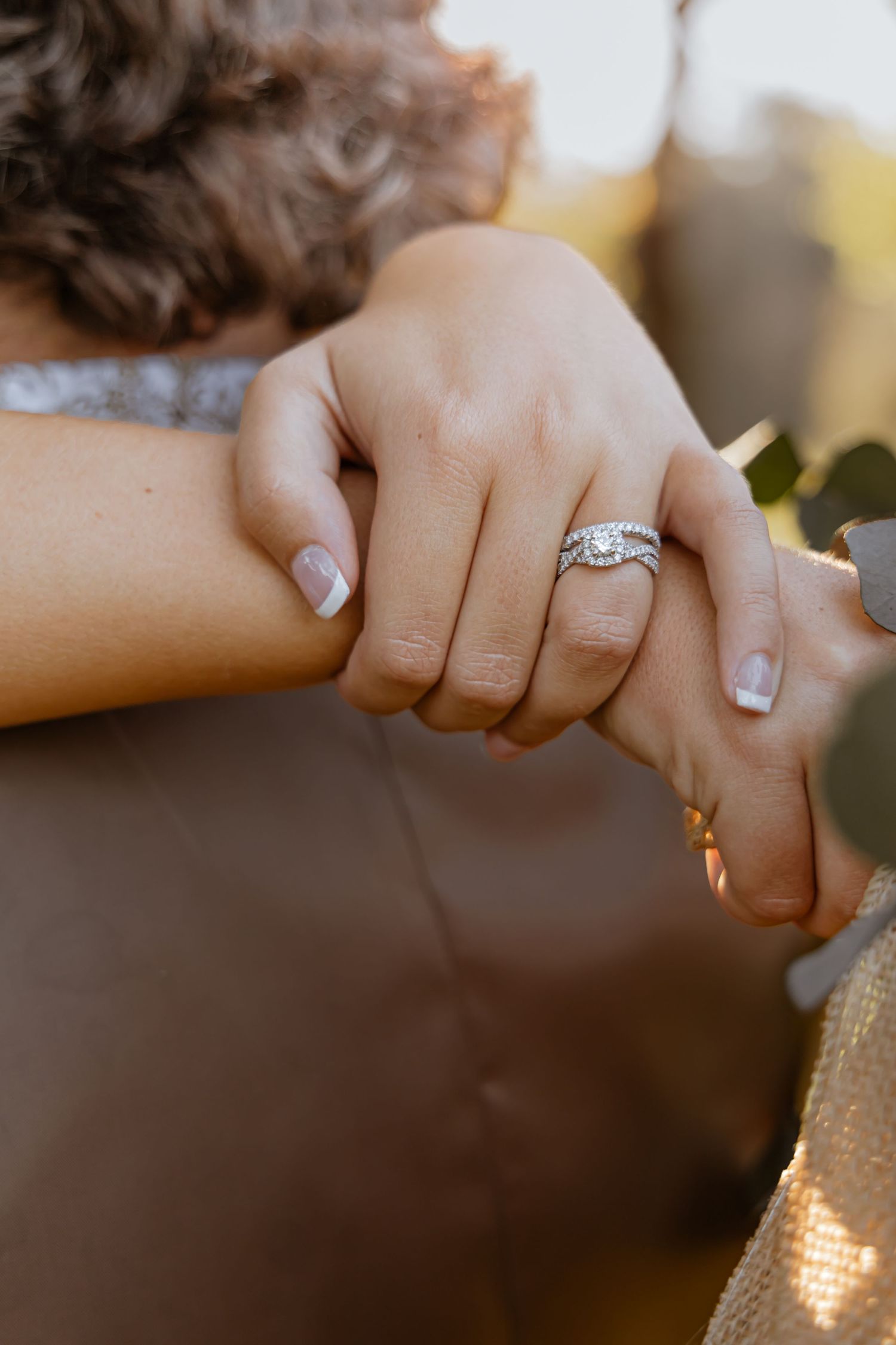 Close-up of hands showing engagement and wedding rings in natural sunlight.