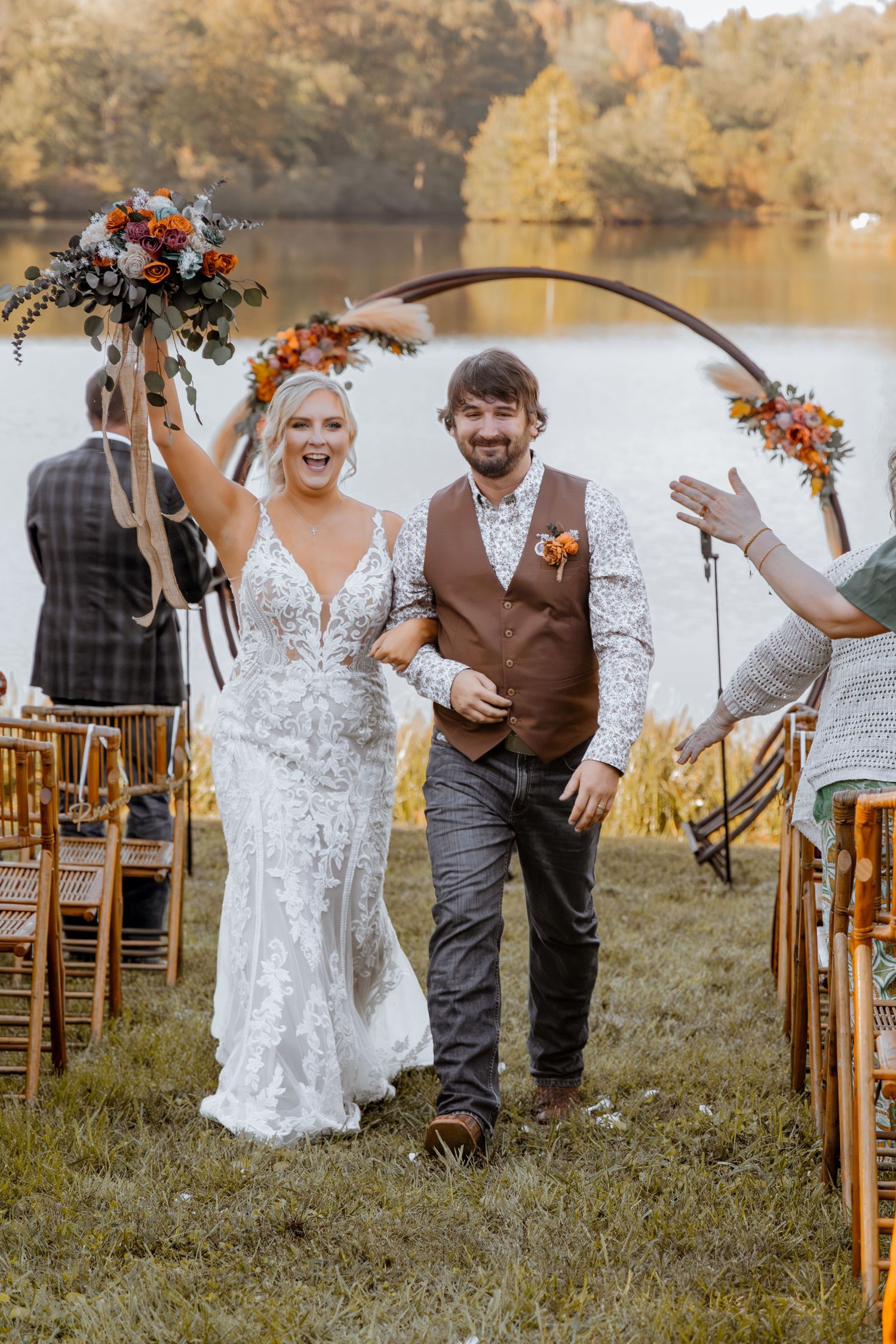 Joyful wedding celebration with wooden arch and chairs set up by a serene lake.