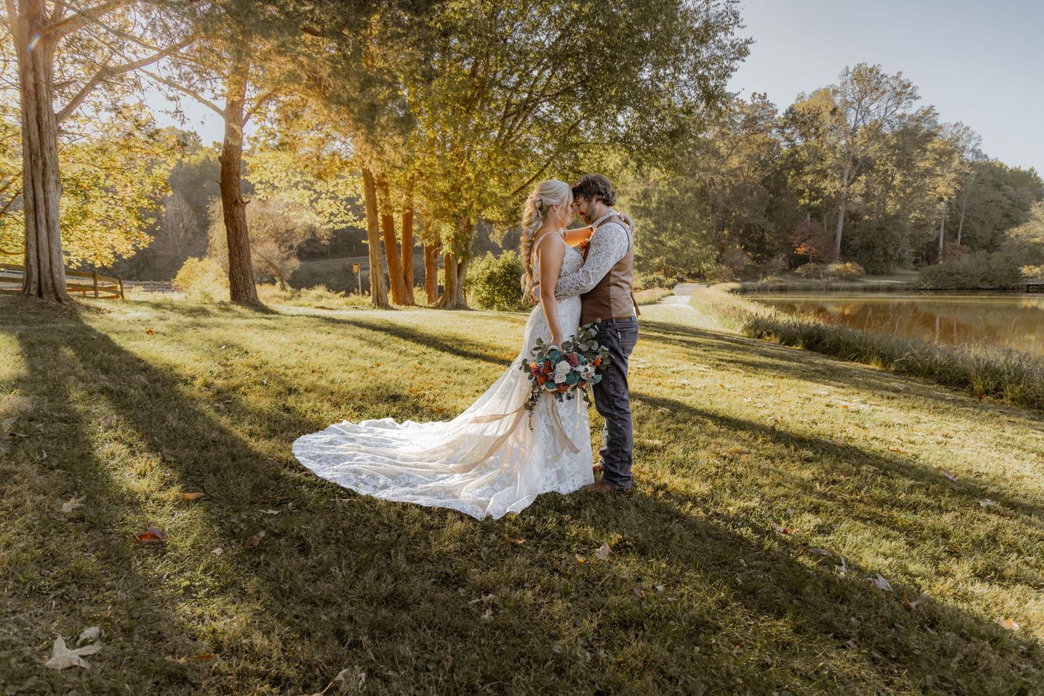 Couple embraces in golden afternoon light with lake and autumn trees in background.