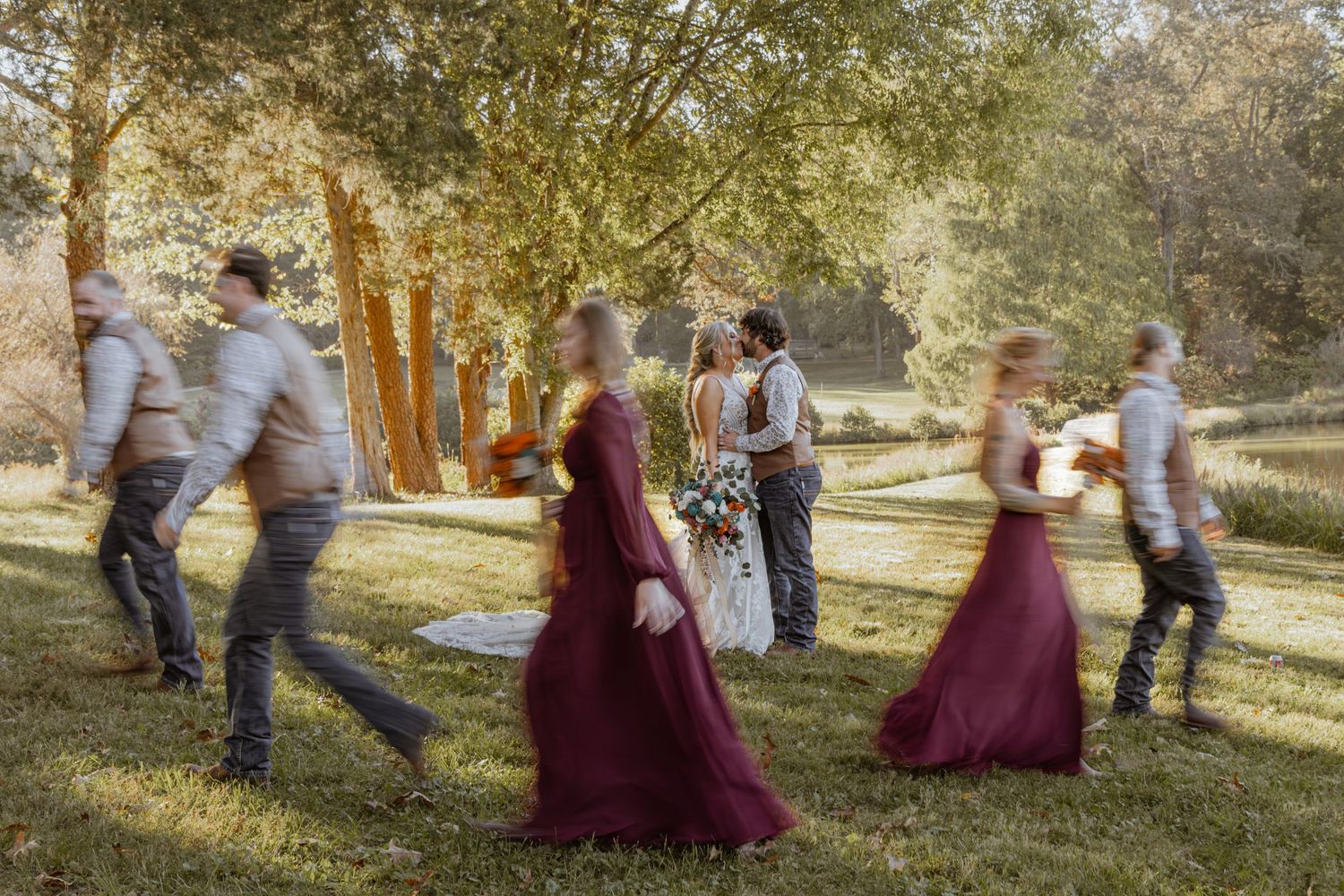 Wedding party enjoying candid moments on grassy hillside during golden hour.