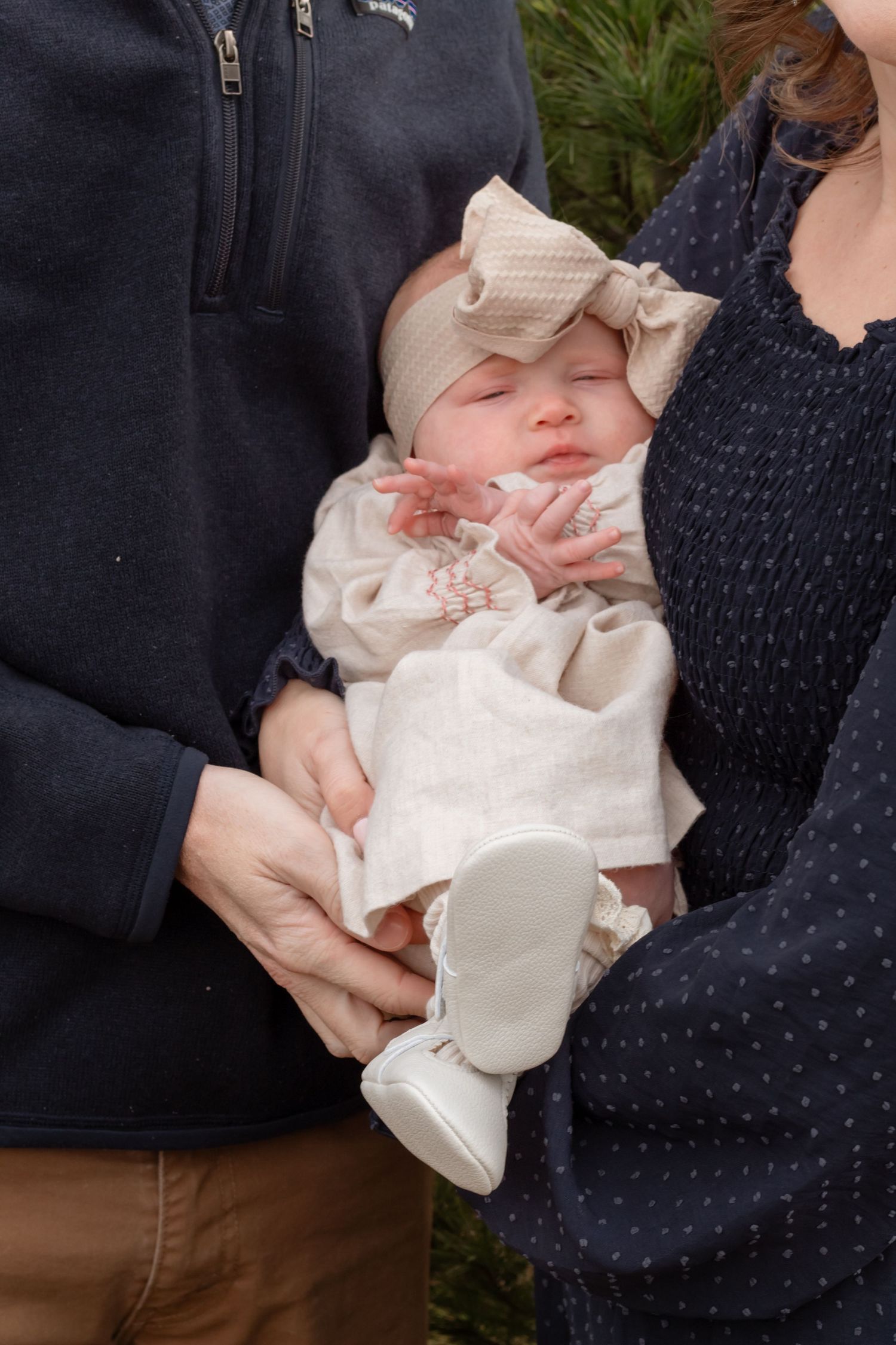 Close-up of baby in white dress being held in navy polka dot clothing.