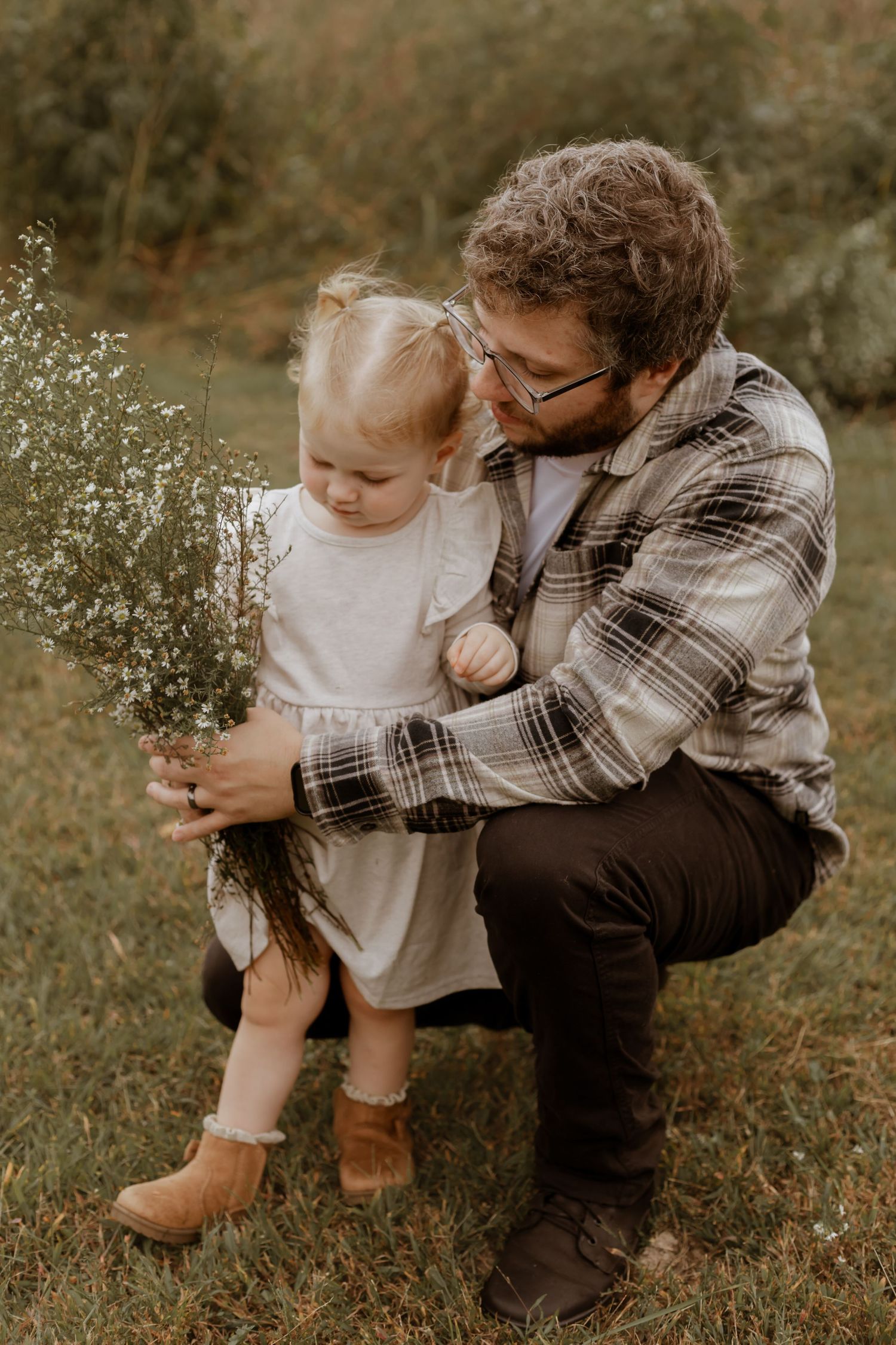 Two people sitting in grass examining delicate white wildflowers together.