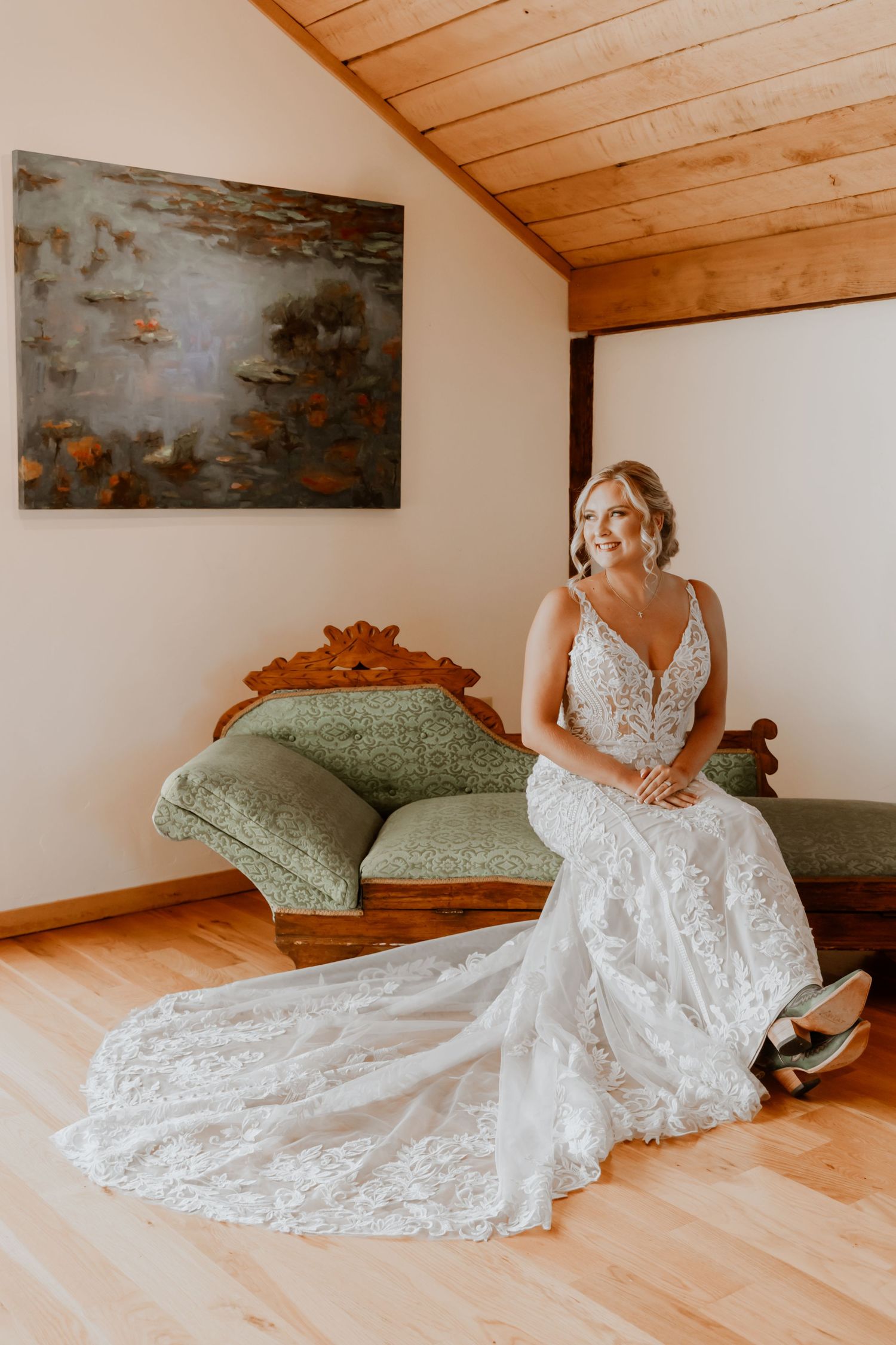 Bride posing on wooden floor showcasing intricate lace wedding gown and train.