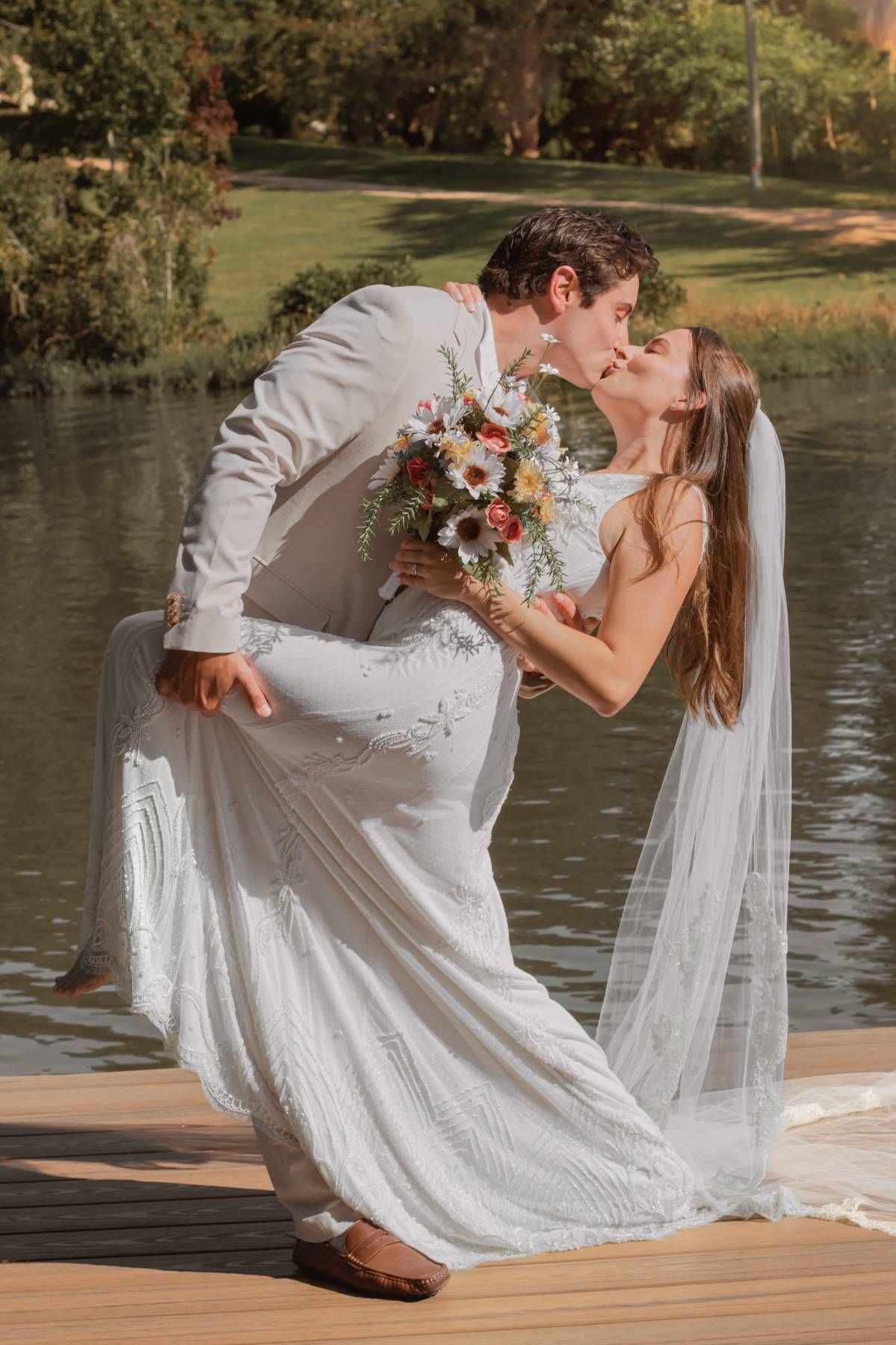 A dramatic dip kiss between newlyweds on a dock with a flowing white veil.