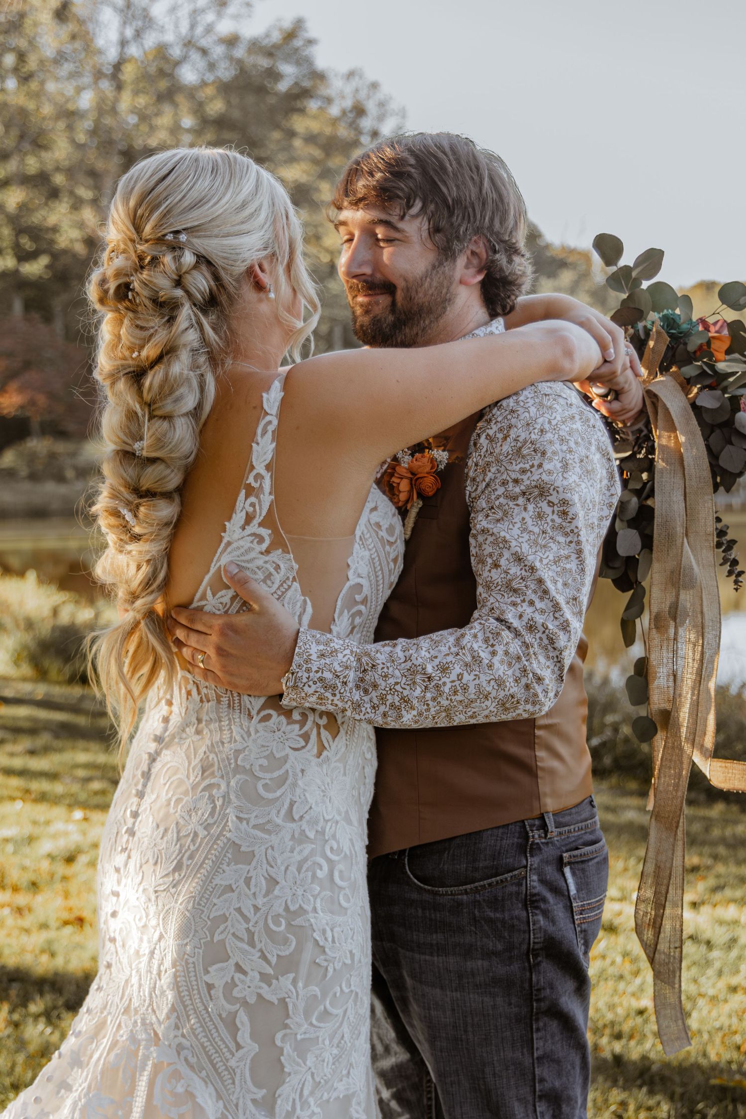 Wedding couple embraces in golden sunlight with rustic farm backdrop.