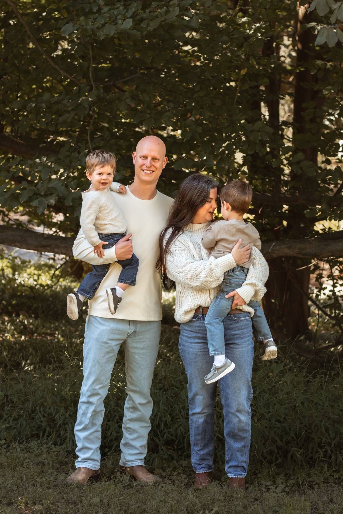 Family of four poses together in coordinating outfits against a wooded backdrop.