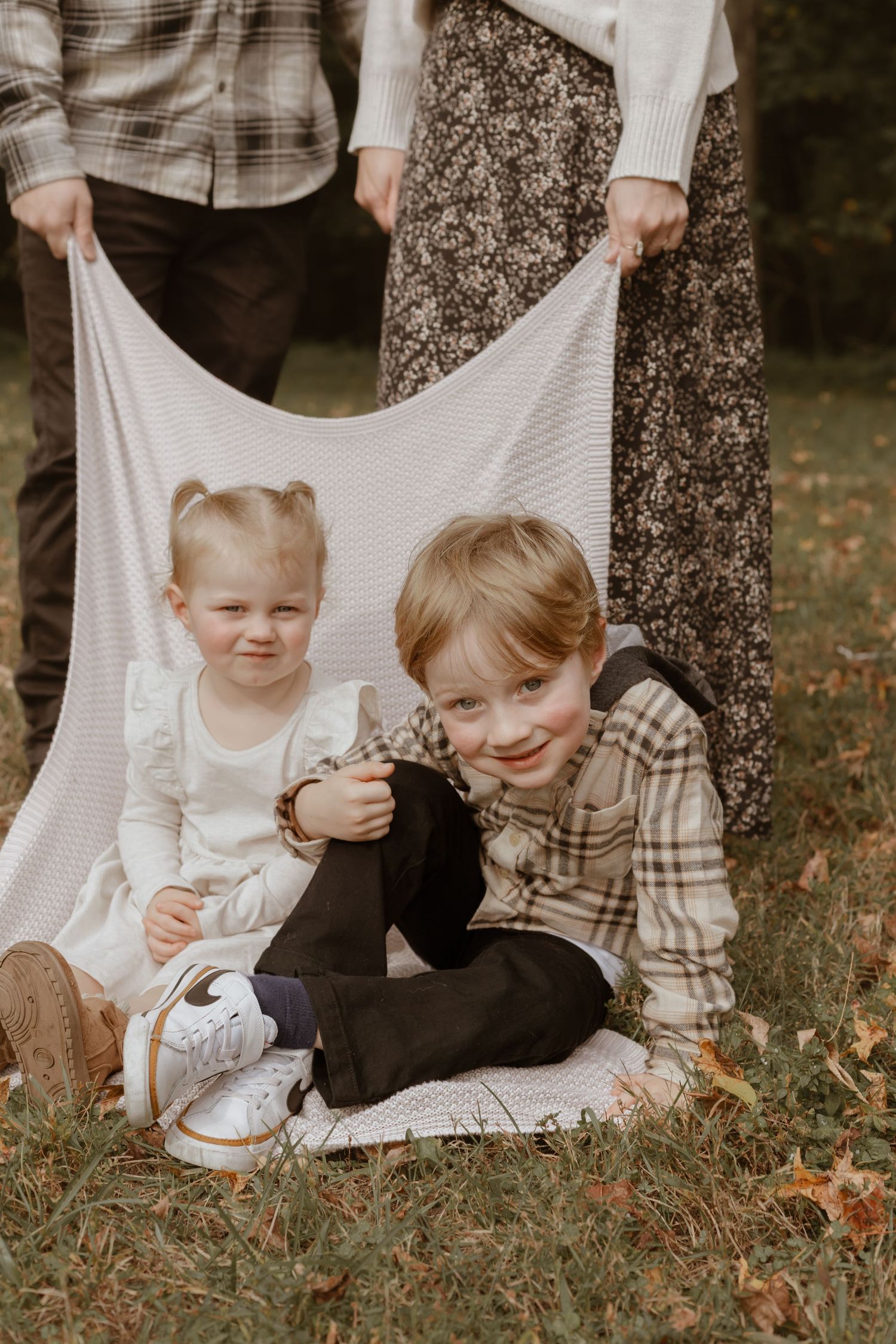 Family sitting together on a white blanket in a wooded autumn setting.
