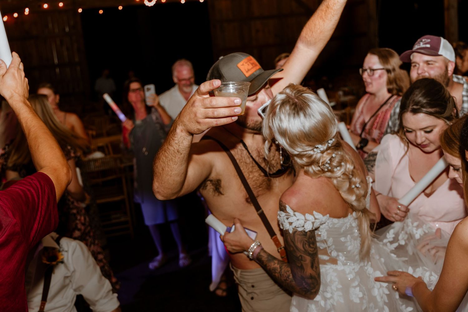 Bride dancing with guests at a lively wedding reception in a rustic barn venue.