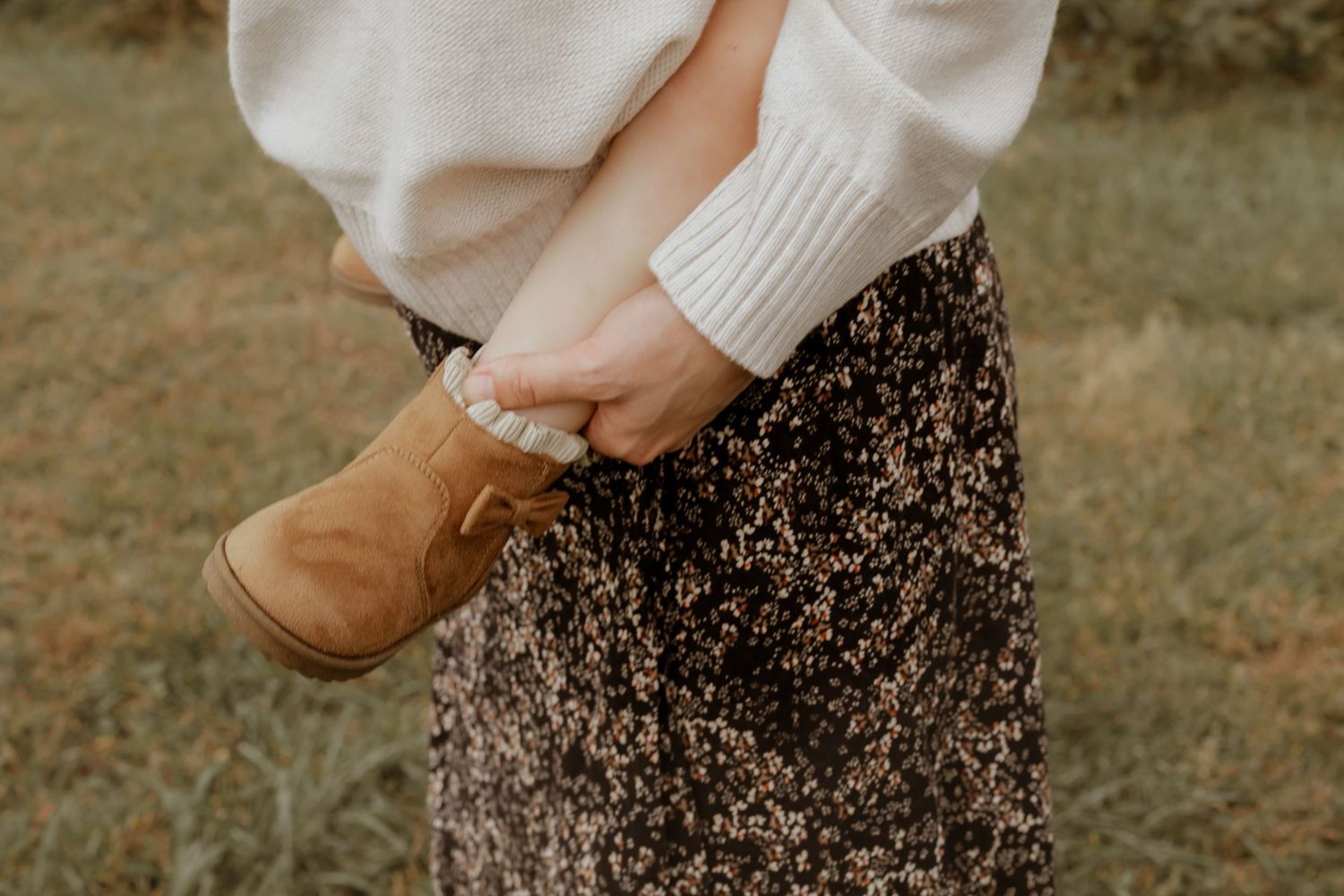 Person wearing brown boots and floral skirt in an outdoor autumn setting.
