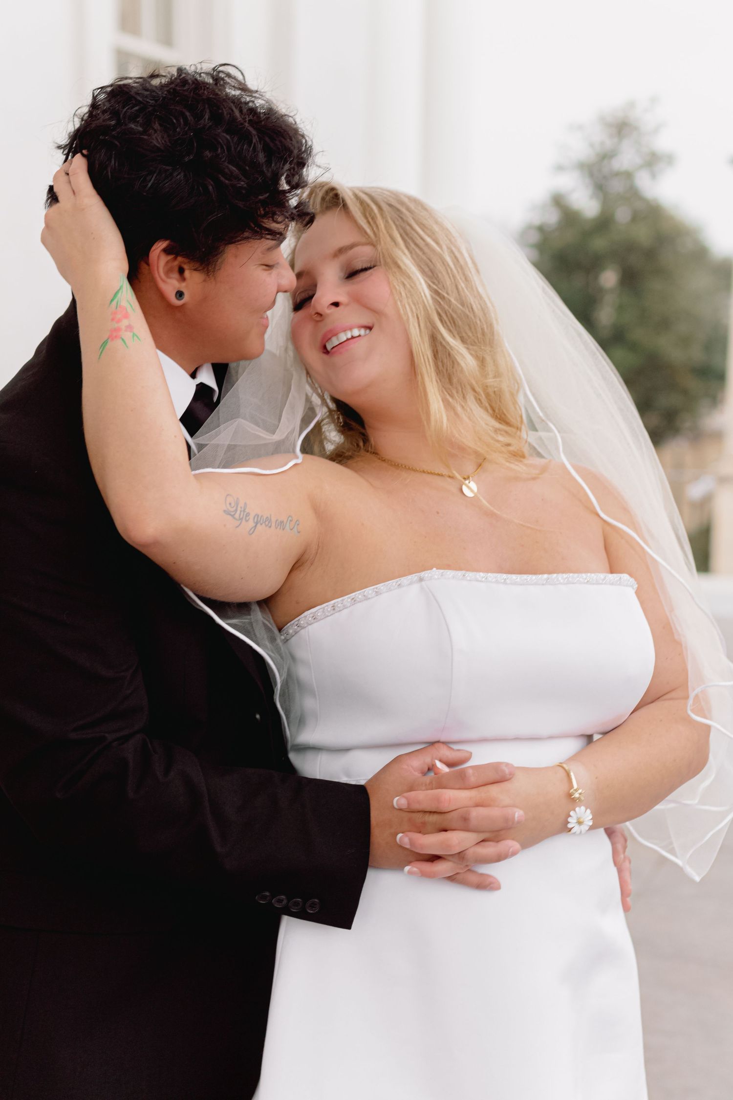 Intimate wedding portrait showing a loving embrace against white architectural backdrop.
