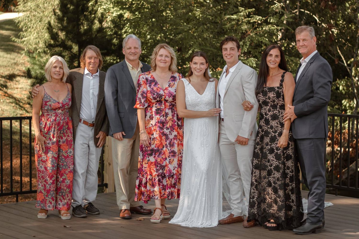 Wedding party in floral dresses and formal attire poses on brick patio.