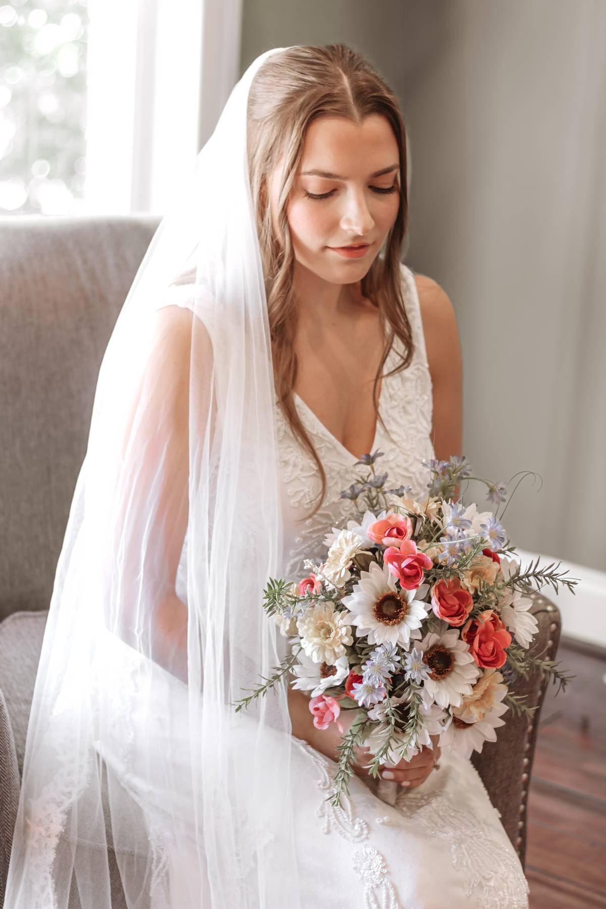 Elegant bride in white lace gown holding a romantic bouquet of pink and white flowers.