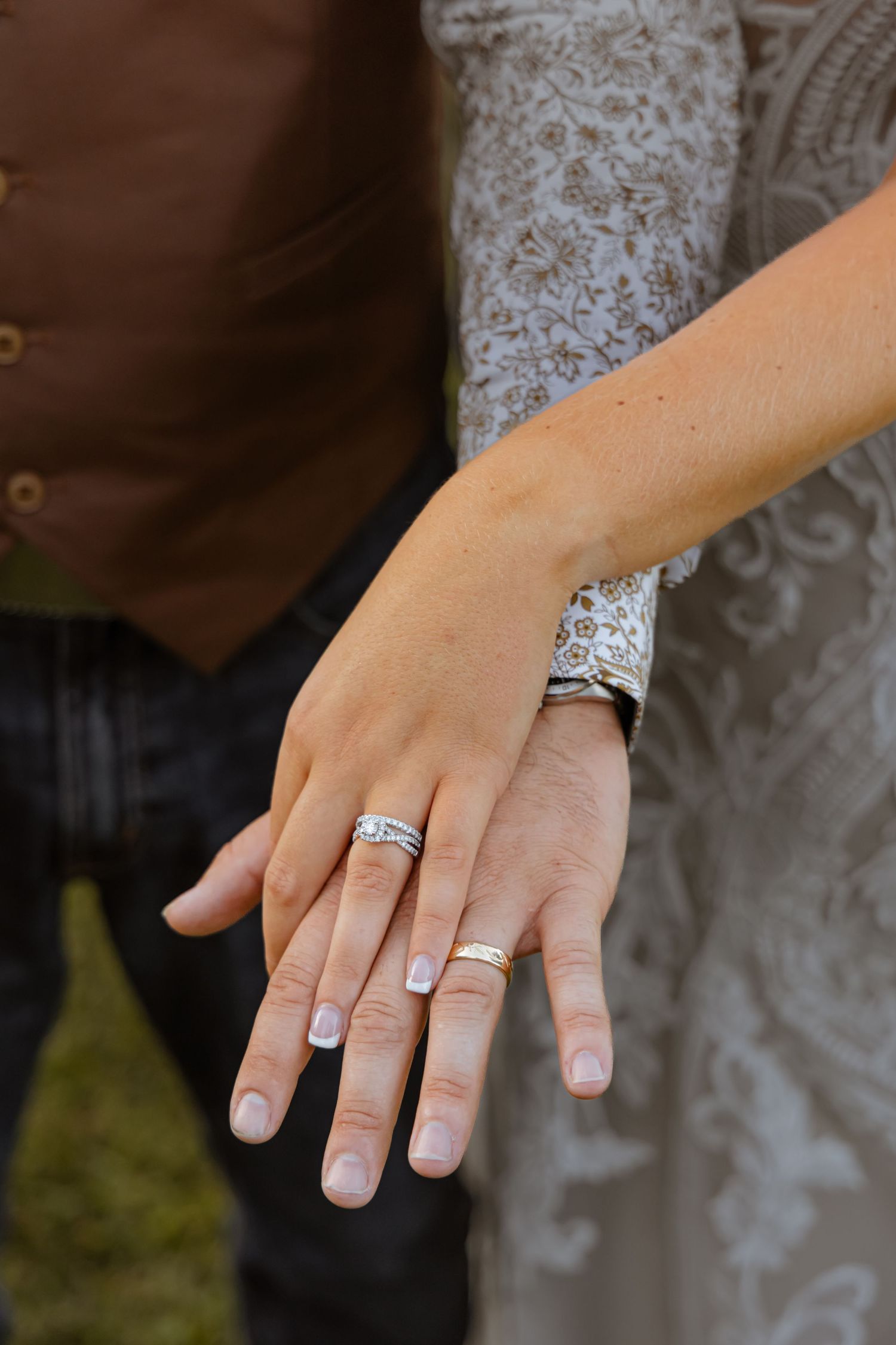Wedding rings displayed on hands with French manicure against lace dress detail.