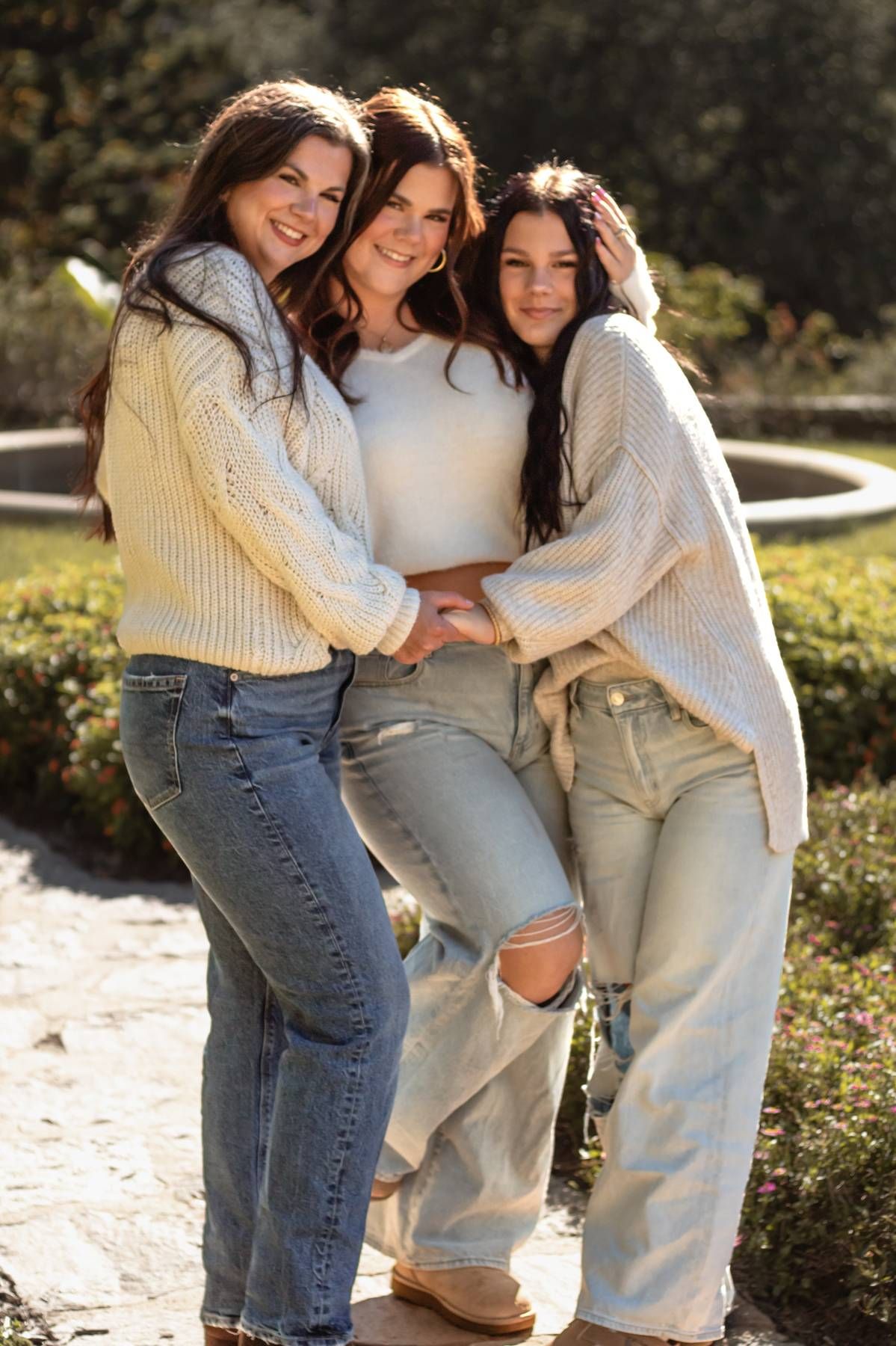 Three friends in casual denim and sweaters laughing together outside.