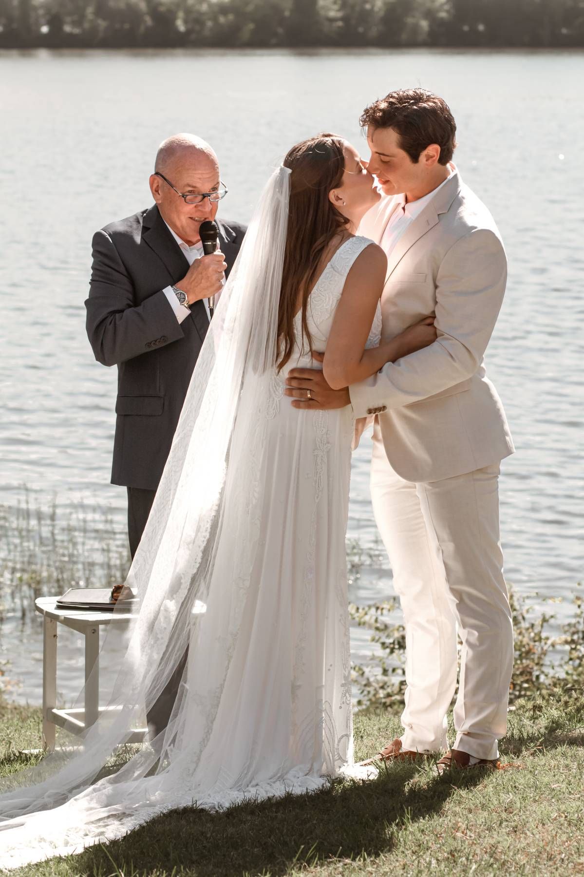 A touching wedding ceremony moment by a lake with the couple and officiant sharing an emotional exchange.