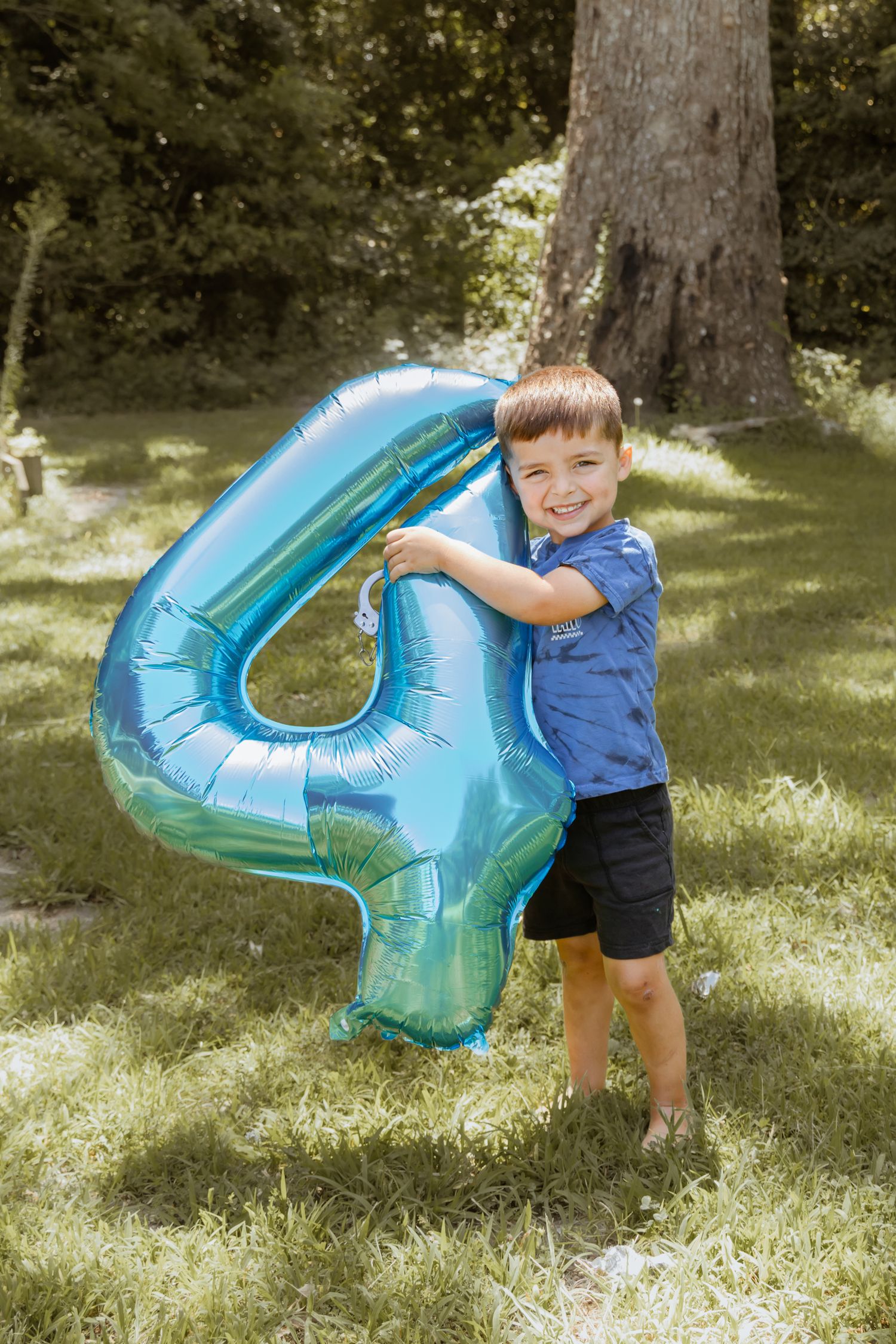 Young child plays with large blue number 4 balloon outdoors.