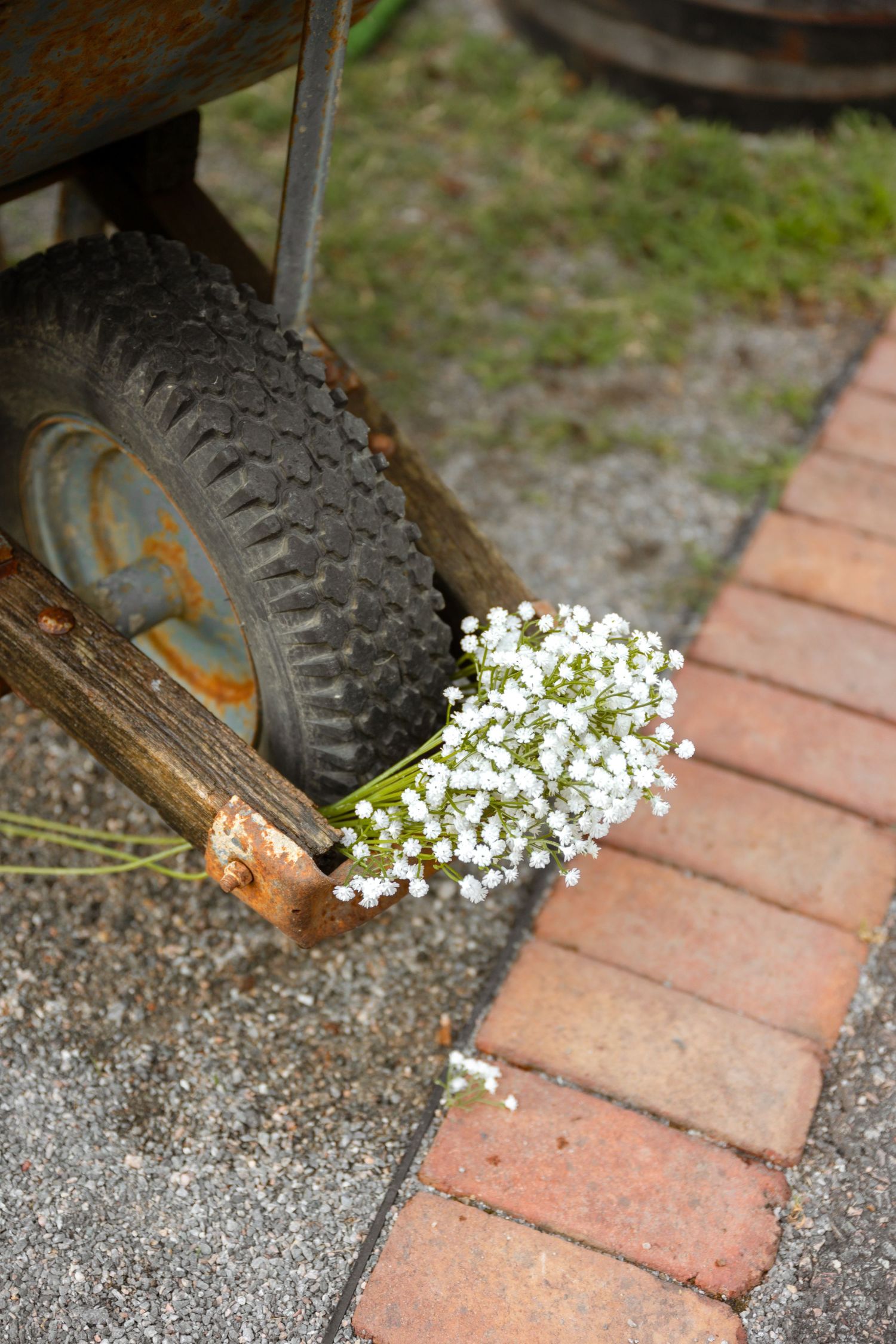 Baby's breath flowers rest against a rustic wheelbarrow wheel on a brick pathway.