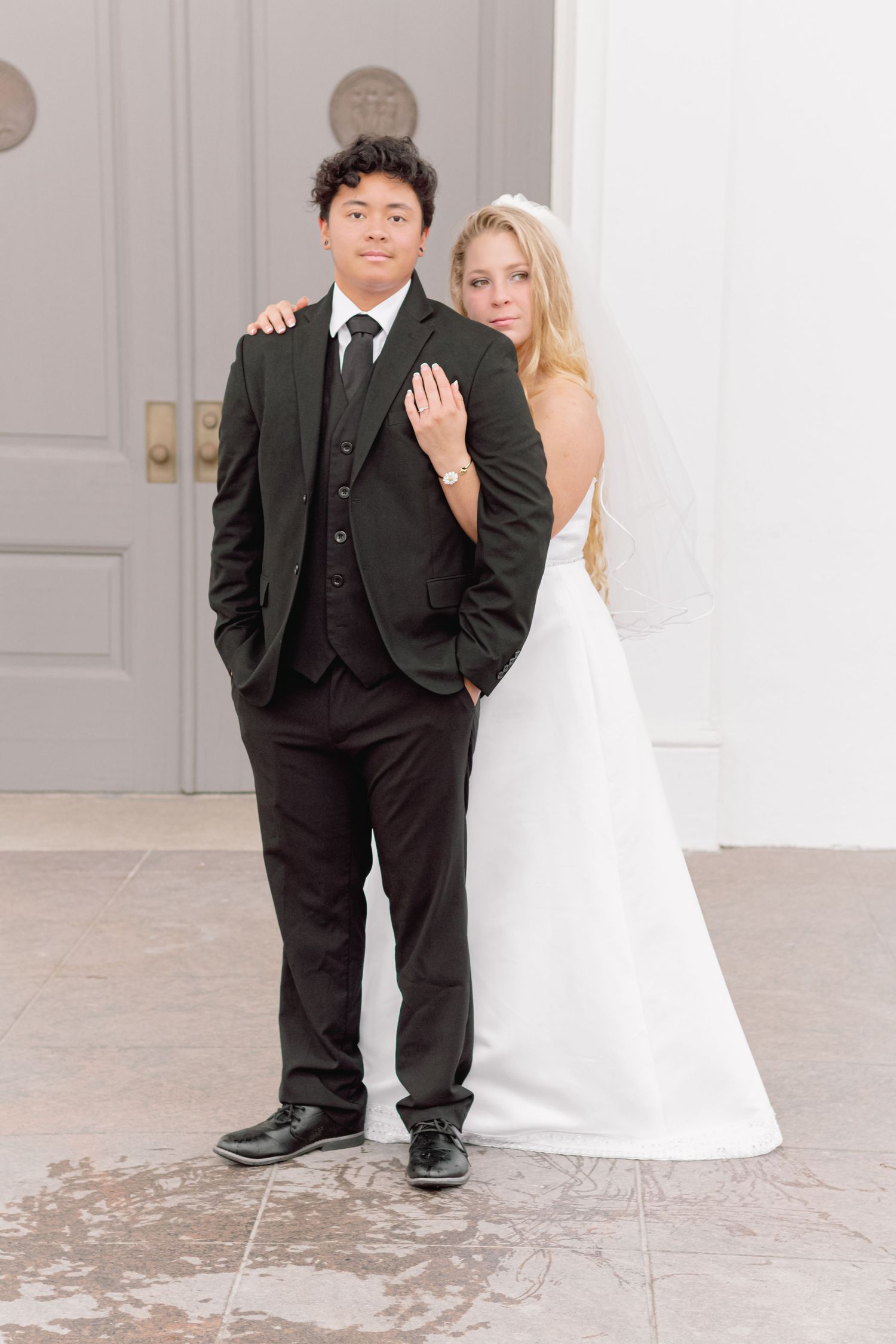 Stylish wedding couple stands together against classic white architectural details.