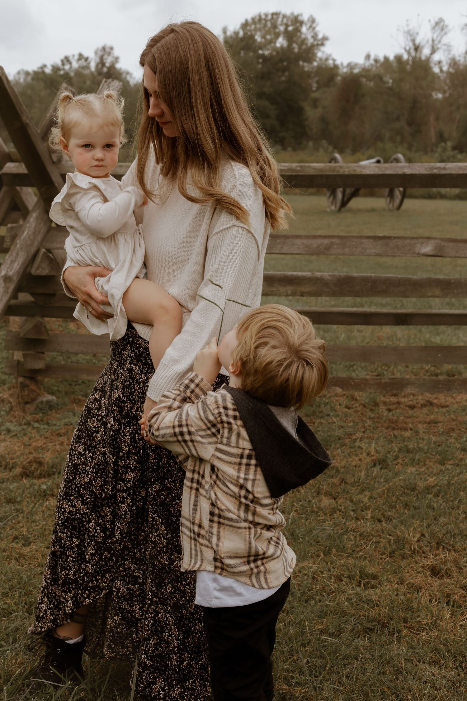 Family members interact playfully in a rustic outdoor setting with wooden fences.
