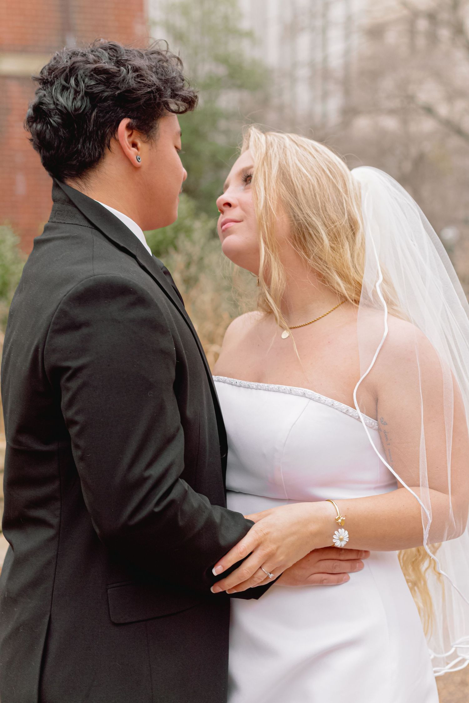 Tender moment between newlyweds captured against brick building backdrop.
