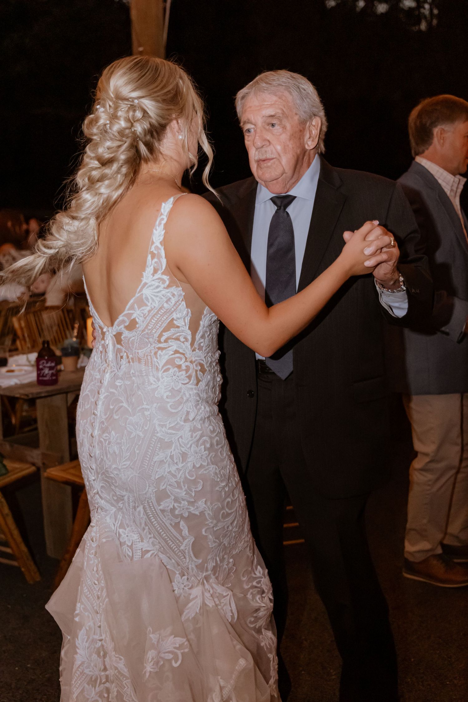 Bride in lace wedding gown shares father-daughter dance at elegant outdoor wedding reception.