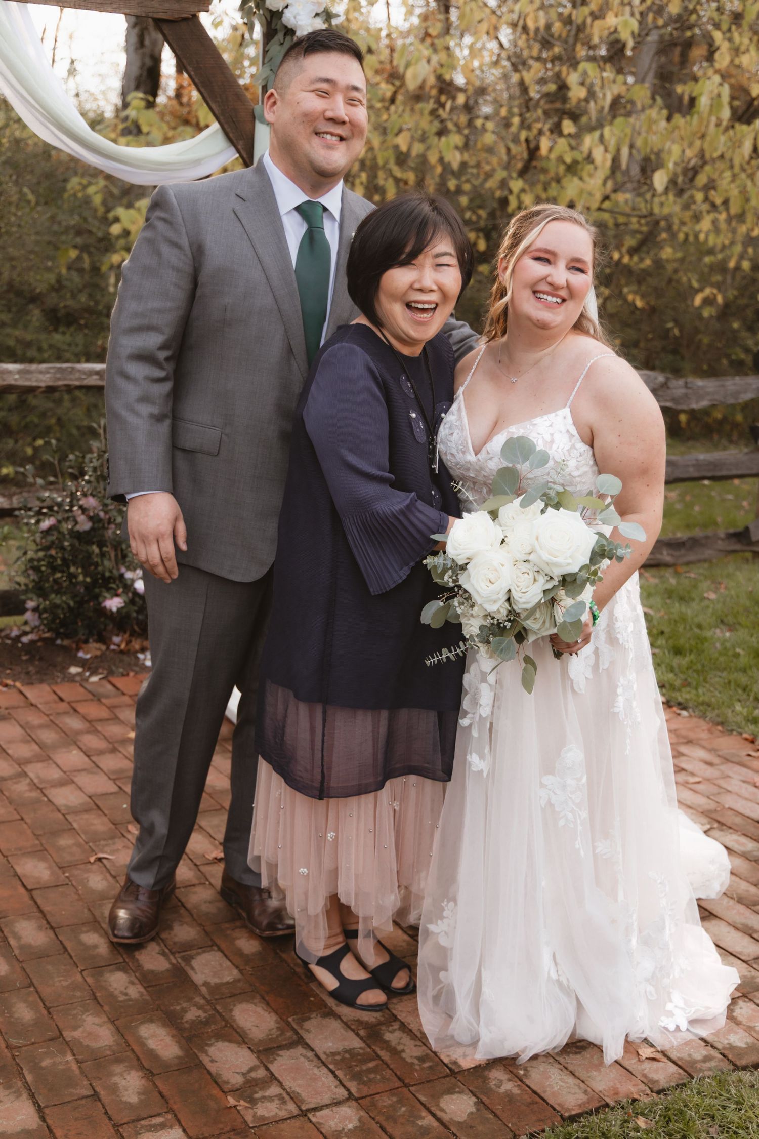 Wedding party gathered on brick patio with white floral bouquets and autumn scenery.