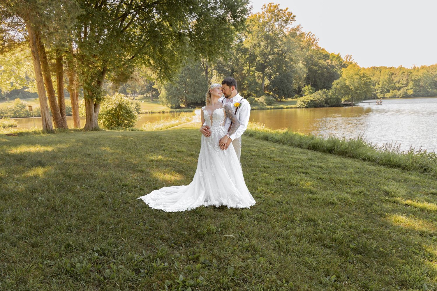 Bride and groom share a romantic kiss in a lush green garden by a serene lake on their wedding day.