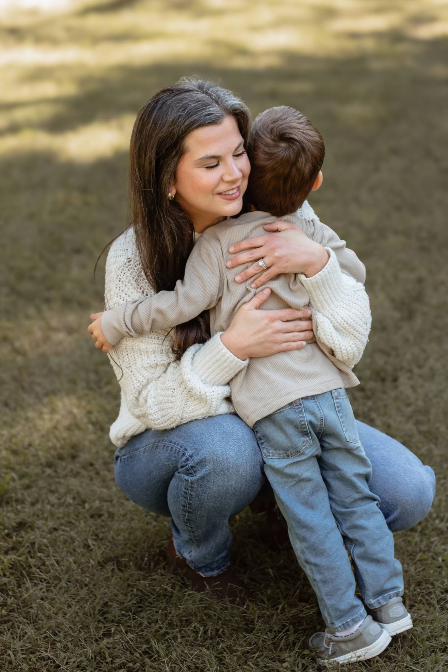 Intimate moment between parent and child sitting together on grass in warm sunlight.