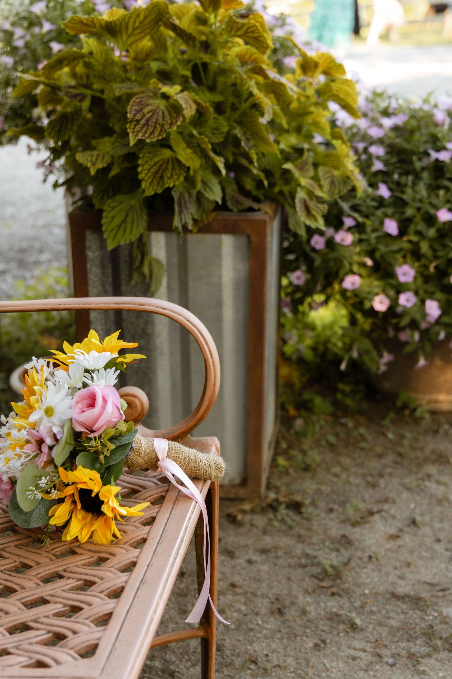 Colorful bridal bouquet with sunflowers and roses resting on vintage metal garden bench outdoors.