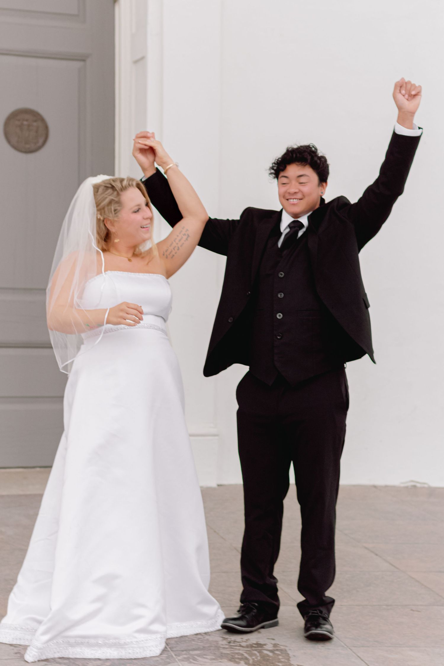 Happy couple celebrates with joyful dancing outside a historic white building.