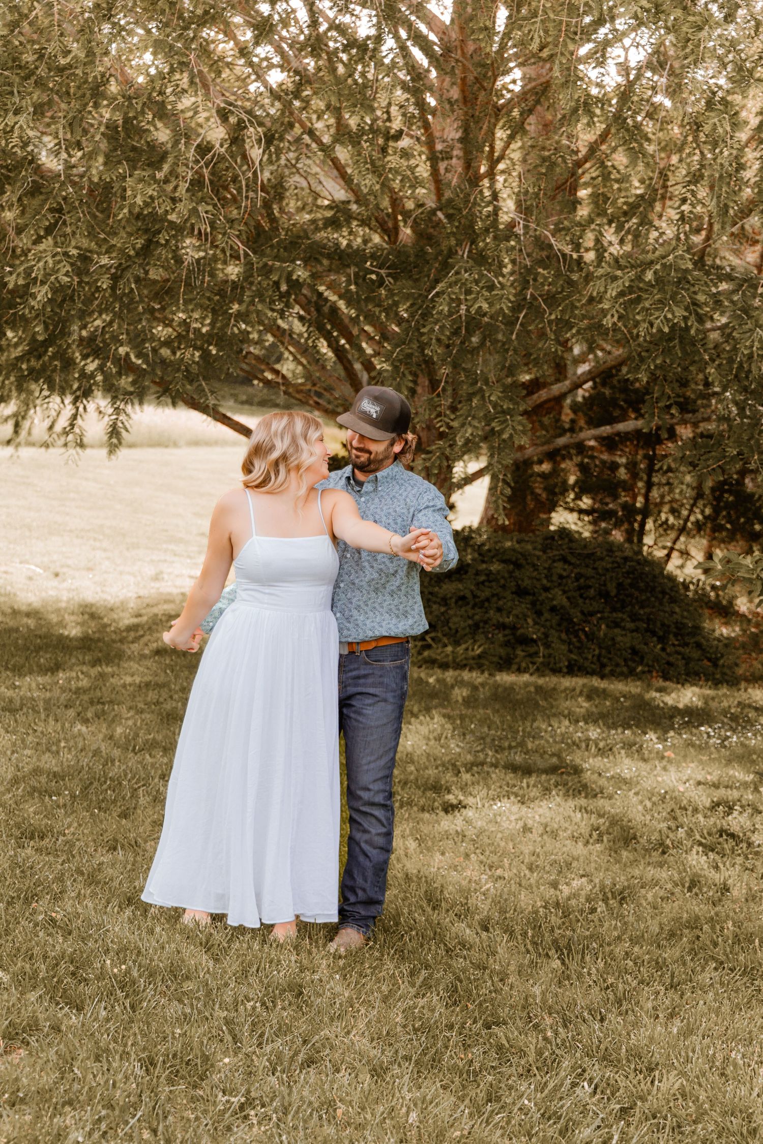 Couple shares tender moment together on grassy hillside in summer light.