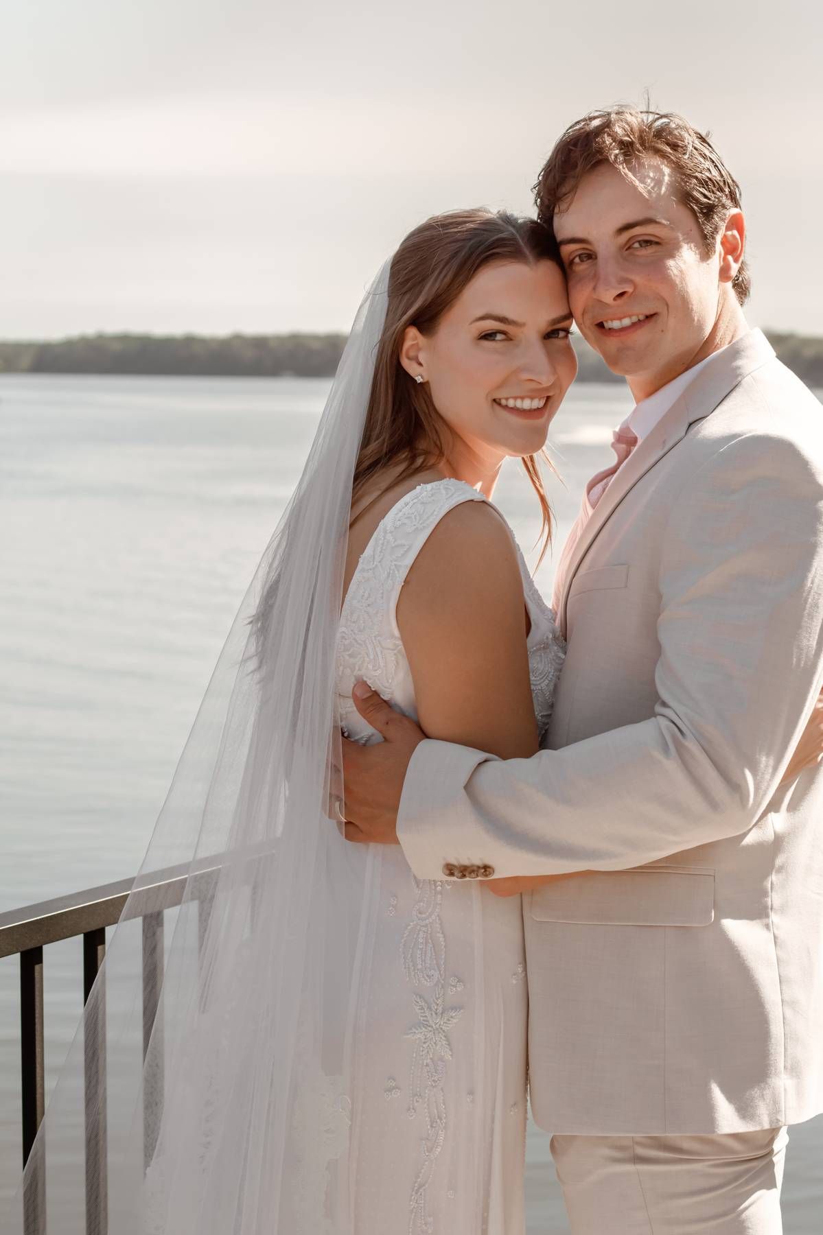 A tender waterfront wedding portrait with a light beige suit and white dress.