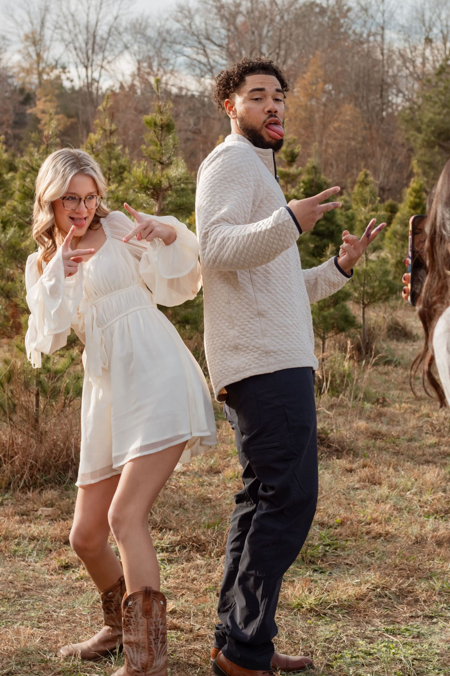 Playful couple dancing together in an outdoor setting with evergreen trees and natural lighting.