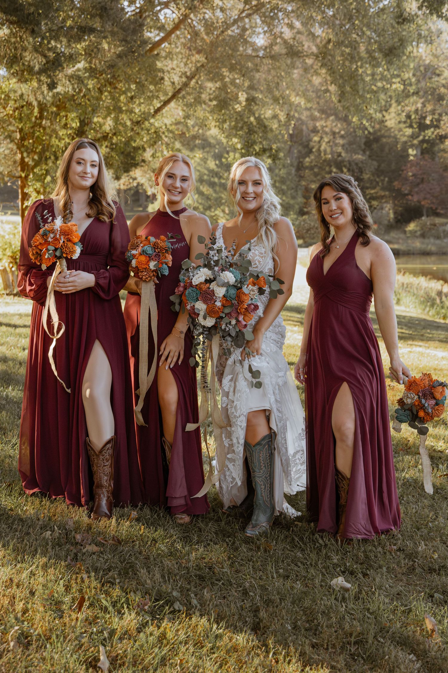 Wedding party in burgundy dresses poses outdoors in golden sunlight for group photos.