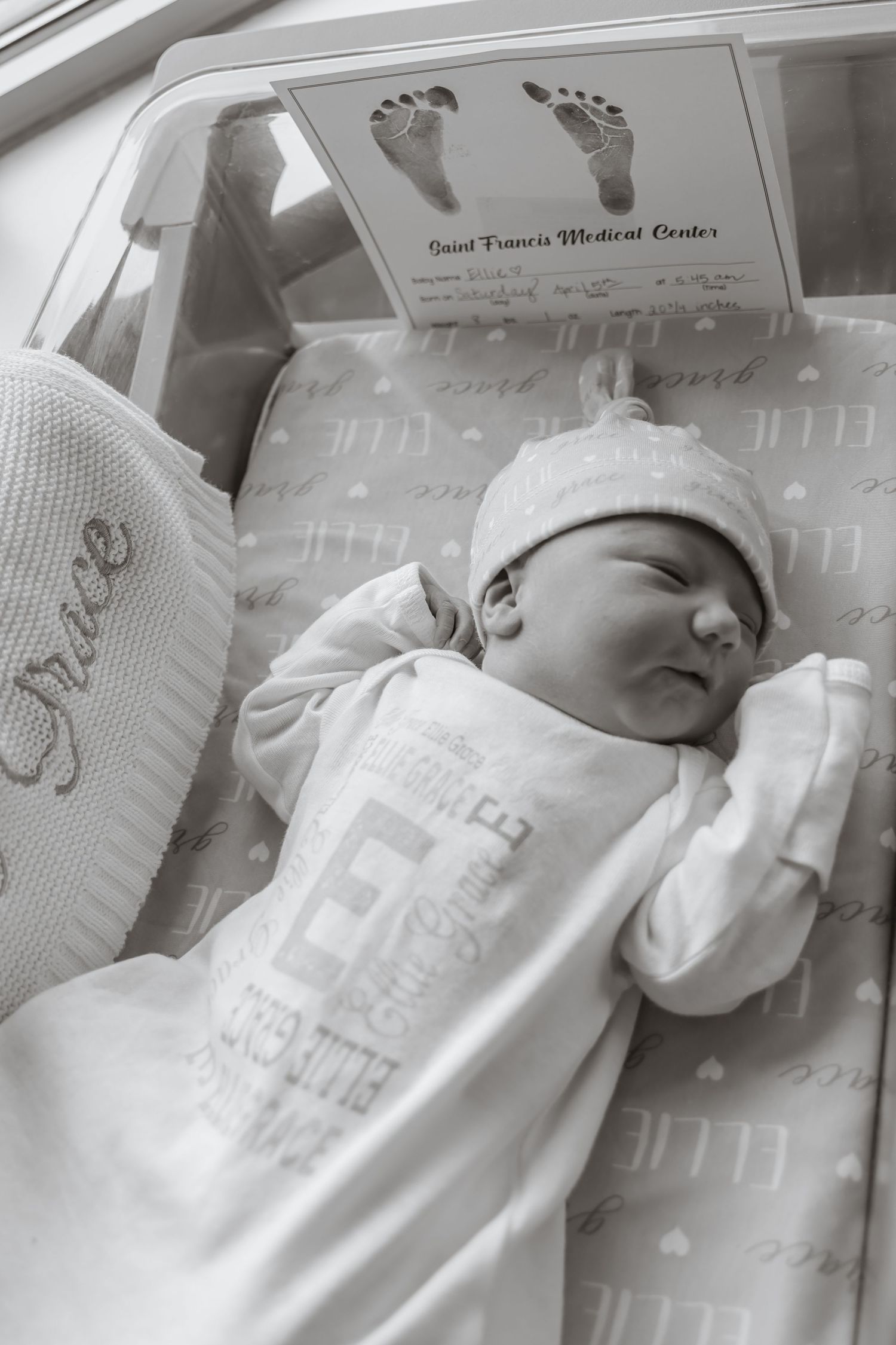 Newborn baby sleeping peacefully in hospital bassinet wrapped in white blanket.