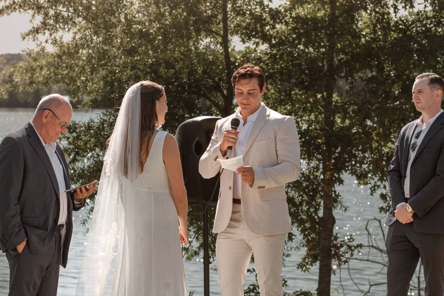 An intimate lakeside wedding ceremony with water and trees in the background.