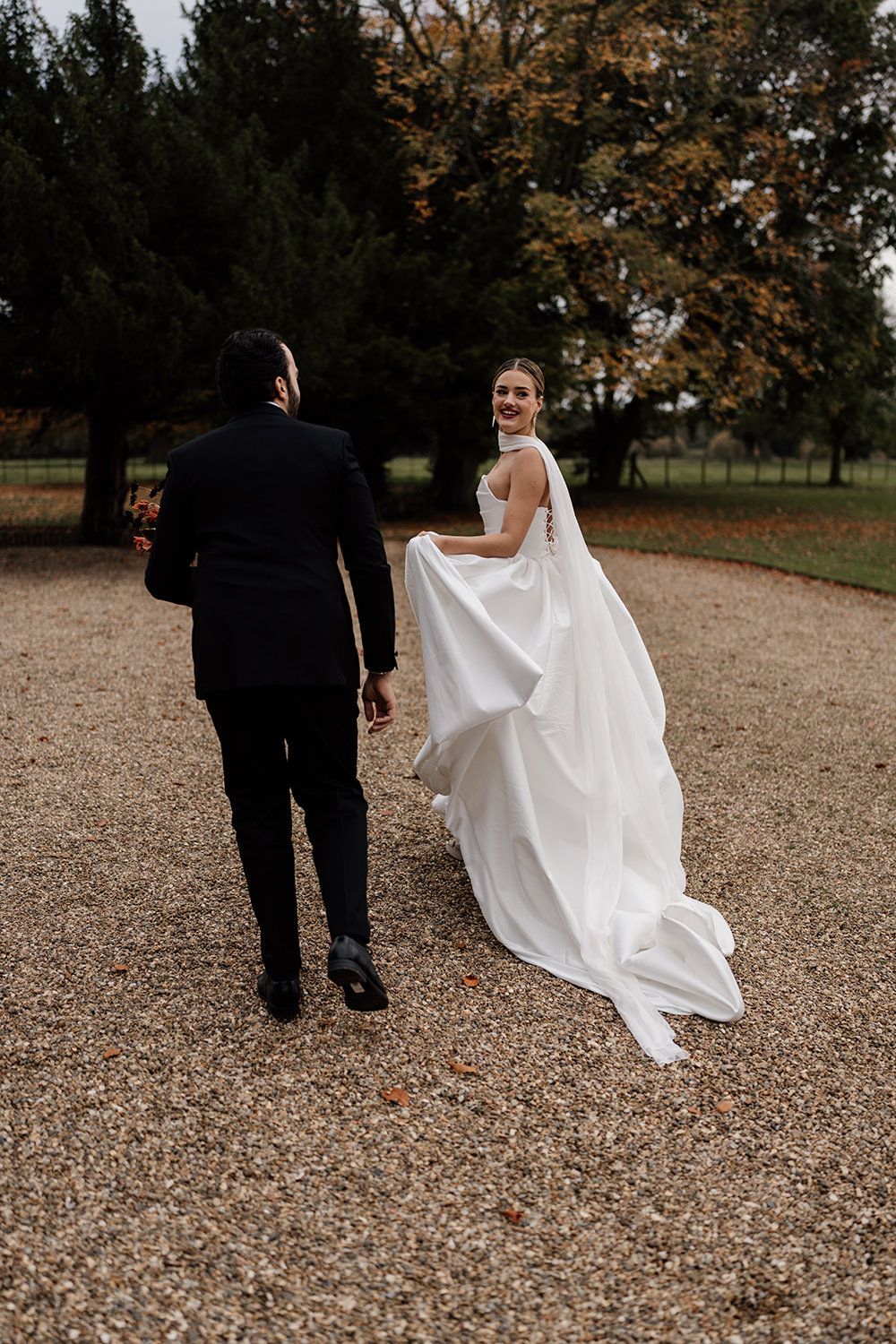 Bride looking behind her while walking with her husband in the grounds of Rise Hall.