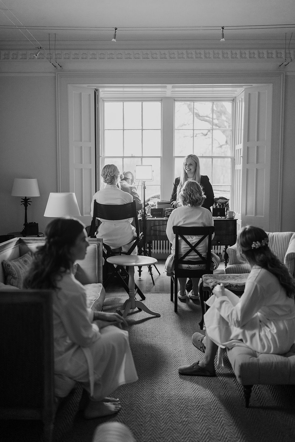 Bride and her mother sat in a chair having wedding makeup done, in-front of a window at Healey Hall.